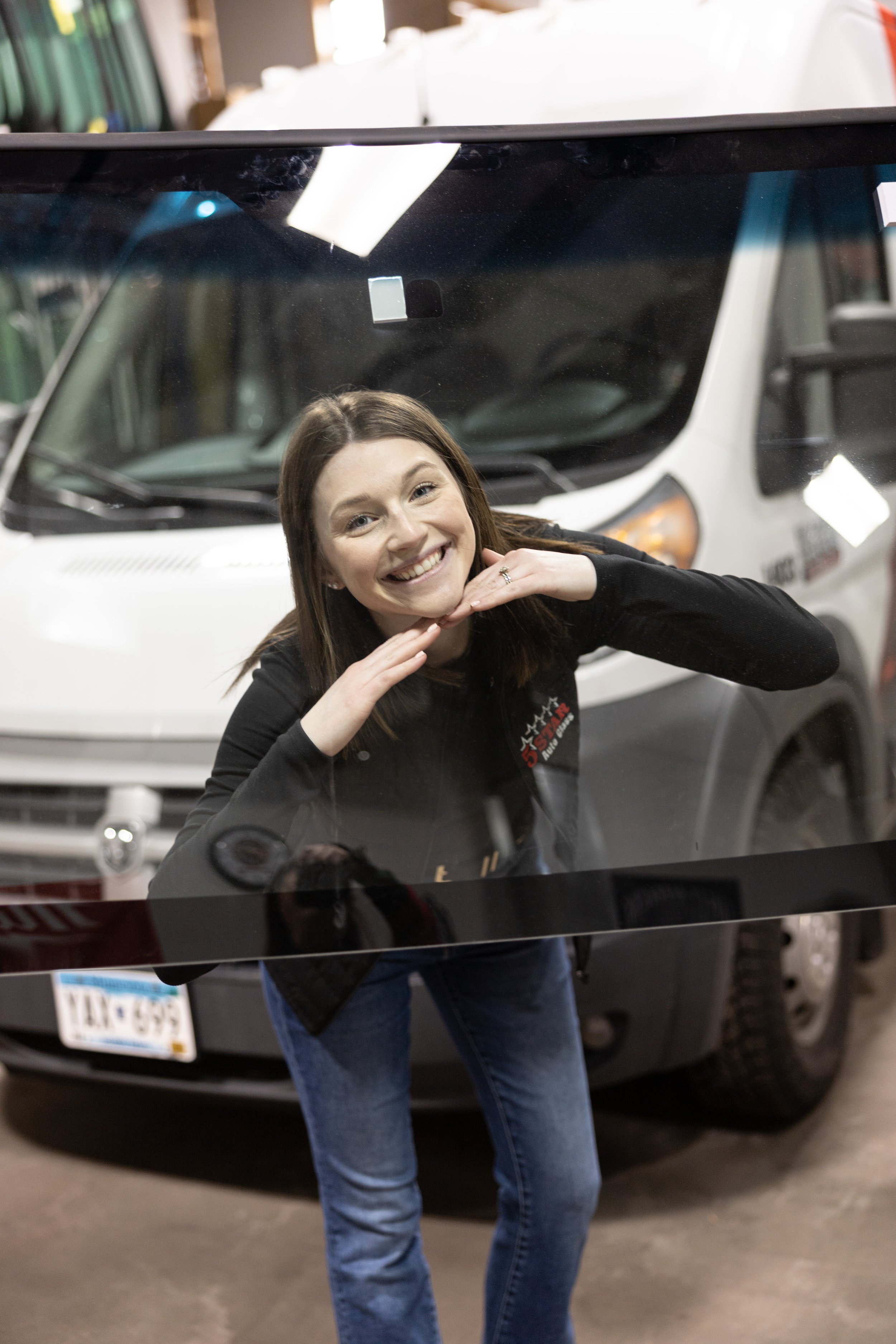 A woman smiling and posing with her face framed by her hands in front of a large truck or van.