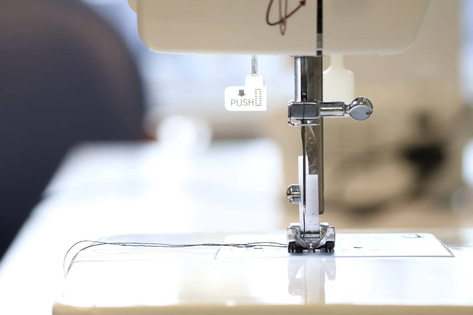 Close-up of a sewing machine needle and presser foot with a tag labeled 'PUSH' above the needle.