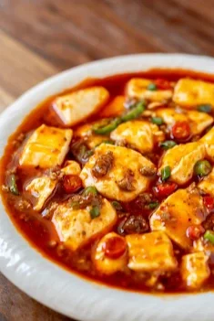A bowl of spicy tofu stew with diced tofu, vegetables, and beans in a red broth.