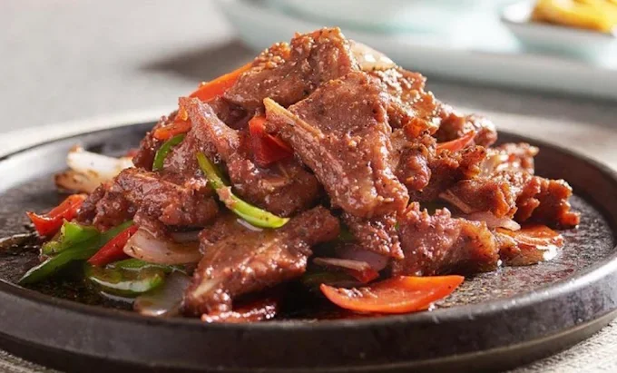 A plate of cooked beef stir-fried with sliced red and green bell peppers and onions