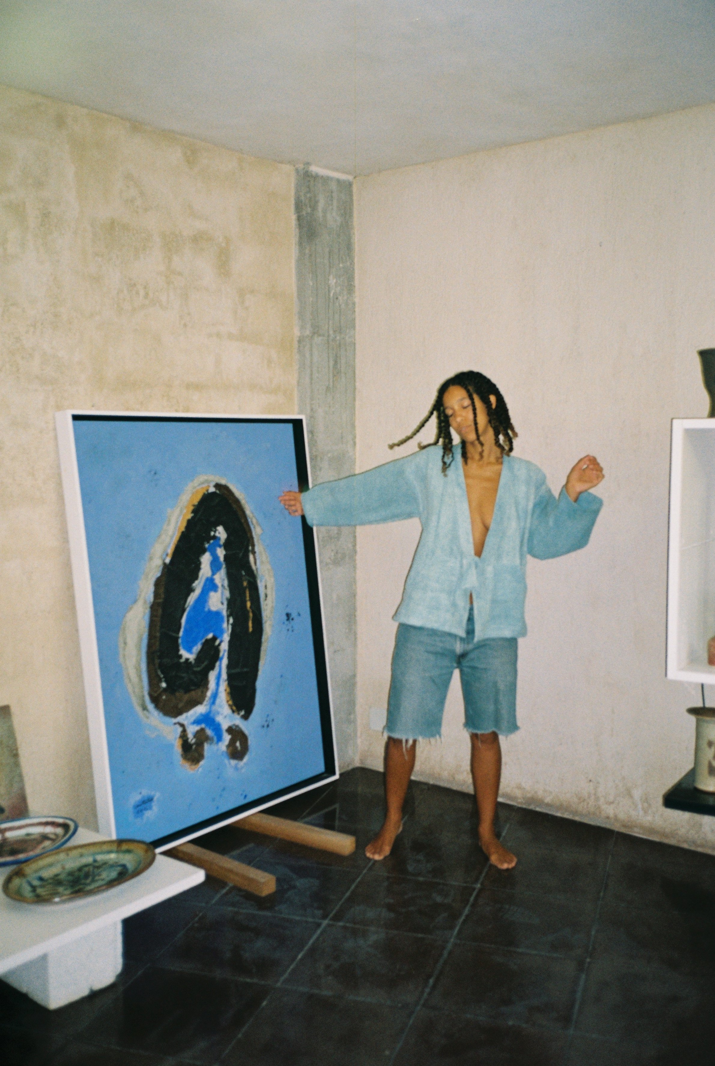 A woman with dreadlocks dancing next to an abstract painting in an art gallery or studio.