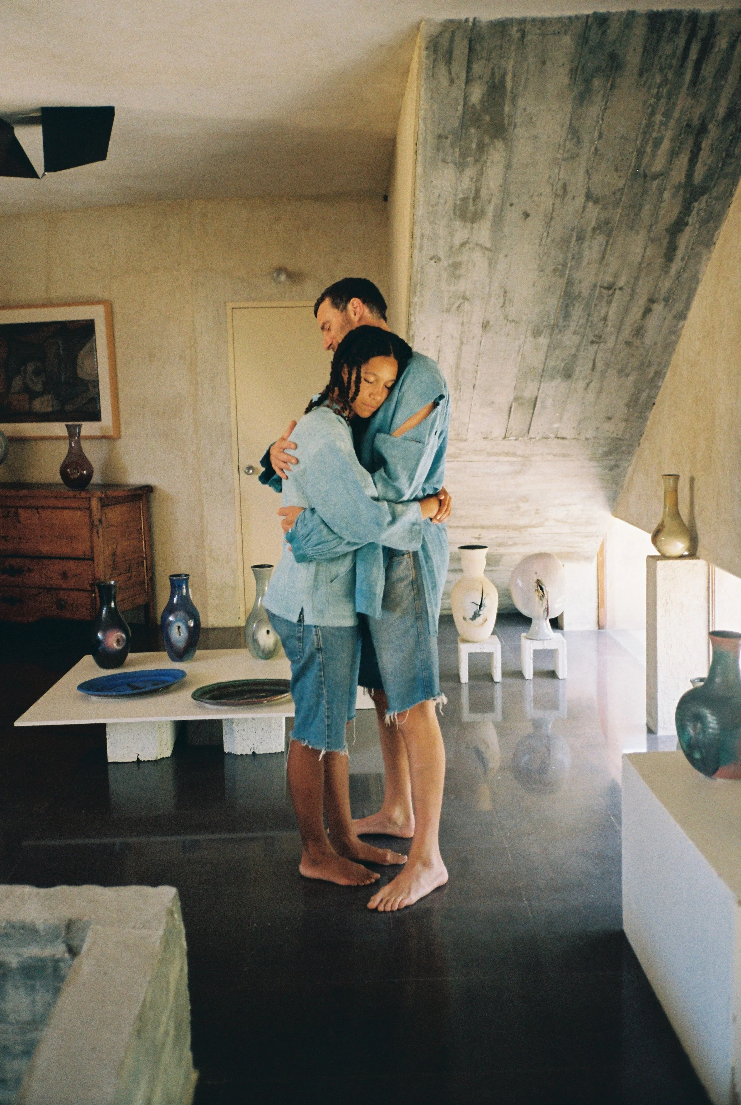Two people embracing in an art gallery, surrounded by vases and sculptures on display.