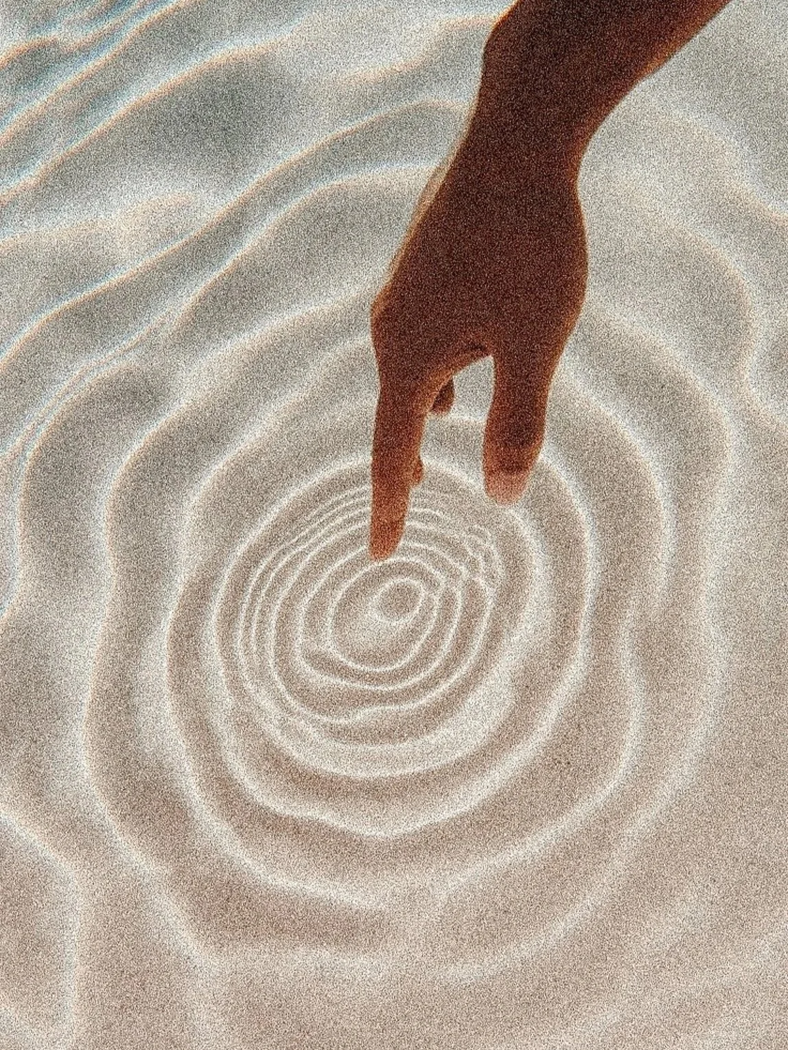Hand pointing at concentric ripple patterns in the sand.