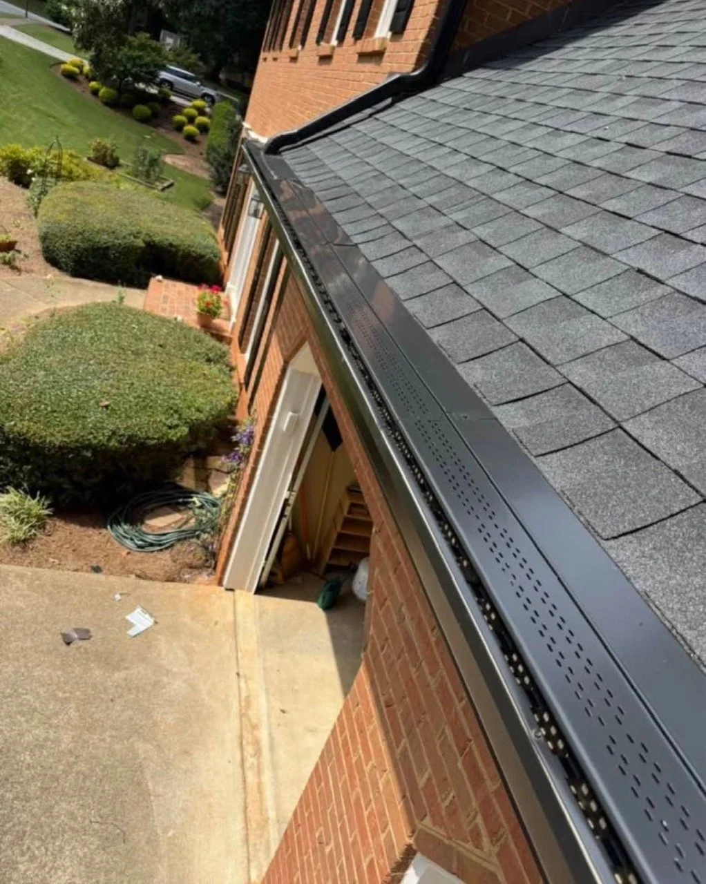 View of a residential house's roof with new black gutters and gray shingle roofing, viewed from above.