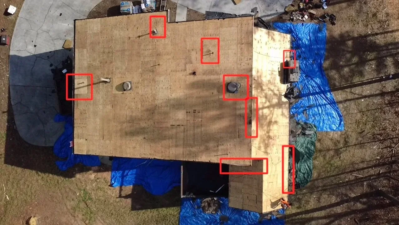 An aerial view of a house under construction, with a wooden roof and blue tarps around the perimeter. Several tools and construction materials are marked with red rectangles.
