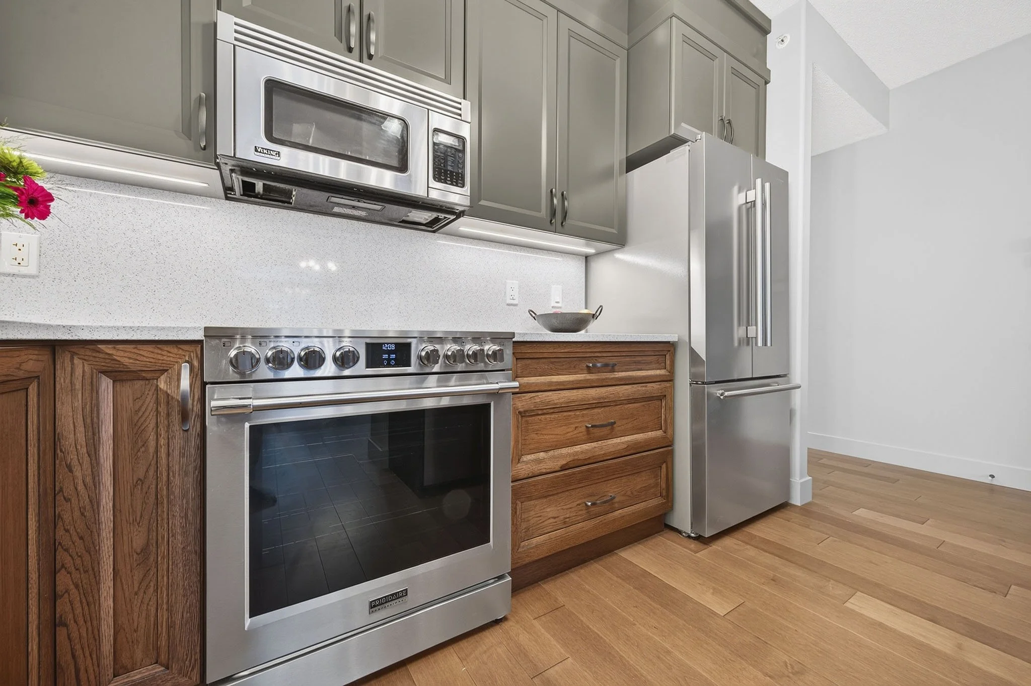 Modern kitchen with stainless steel oven, microwave, and refrigerator, wooden drawers, gray cabinets, and hardwood flooring.
