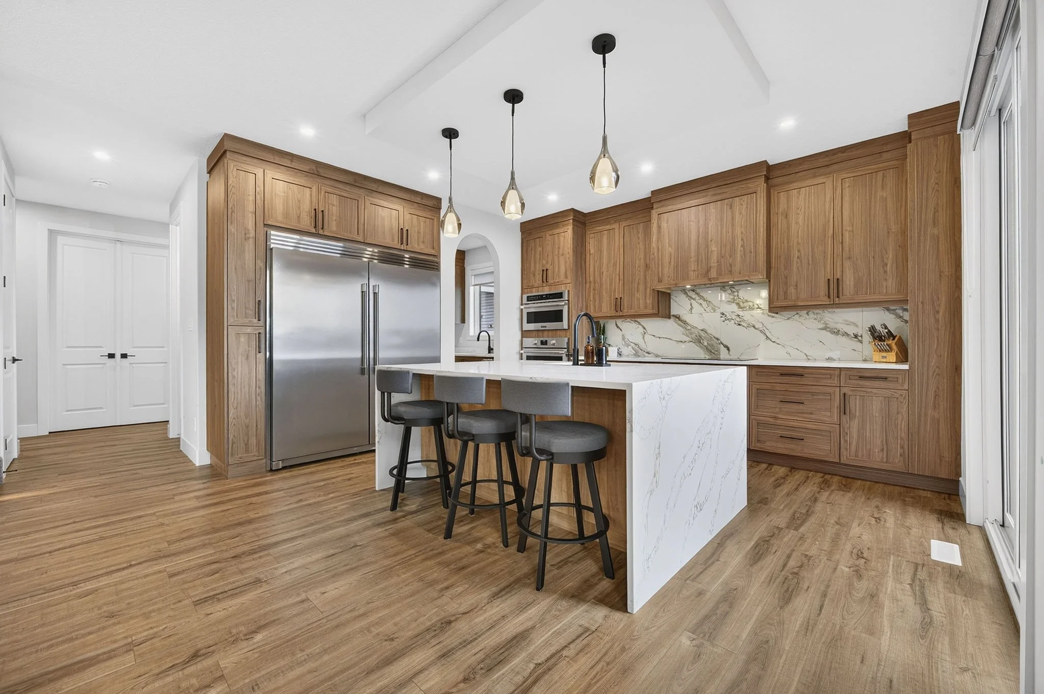 Modern kitchen with wooden cabinets, stainless steel refrigerator, marble island, and three hanging pendant lights