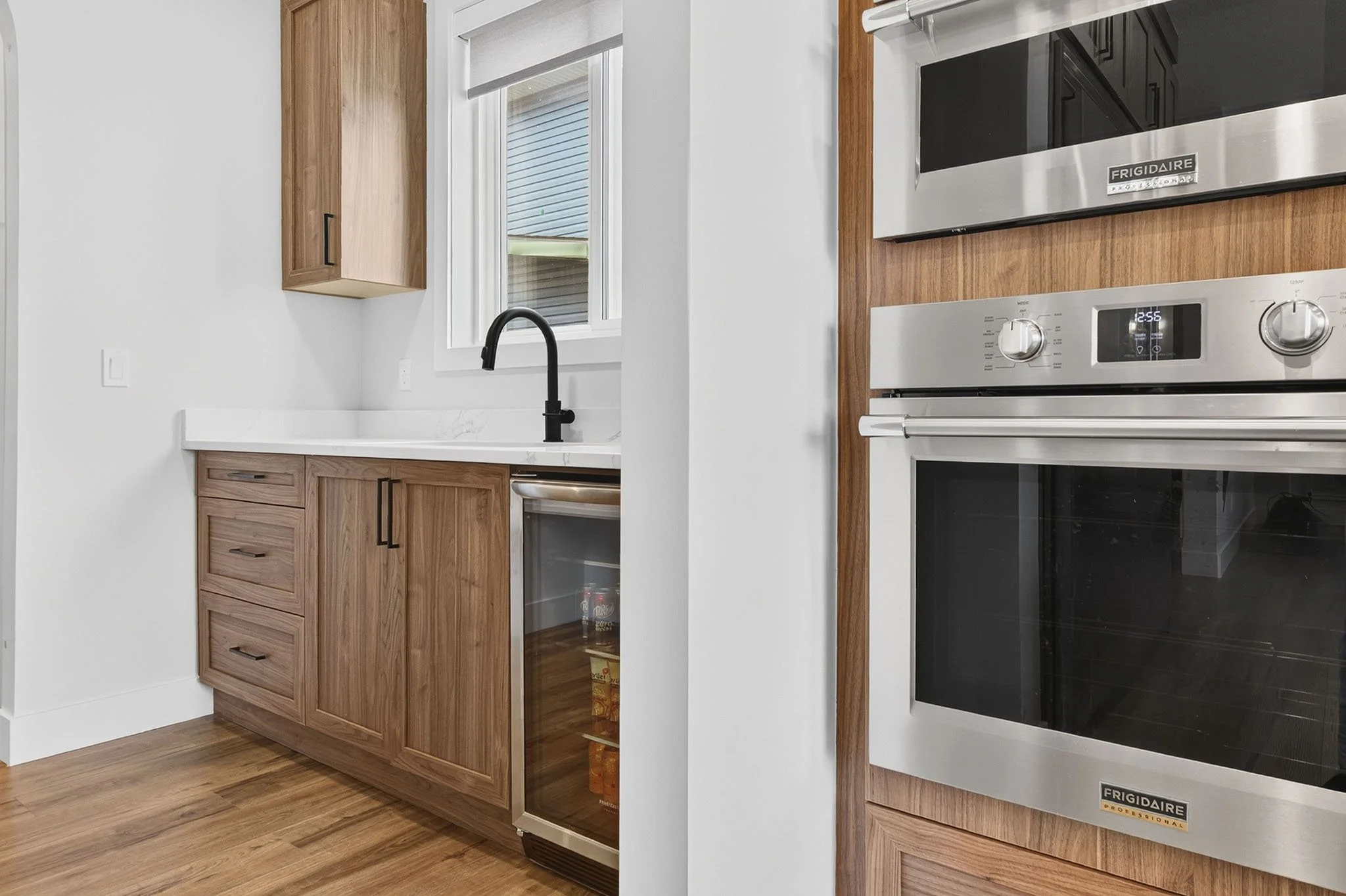 Kitchen with wooden cabinets, black faucet, window with blinds, and a stainless steel Frigidaire oven.