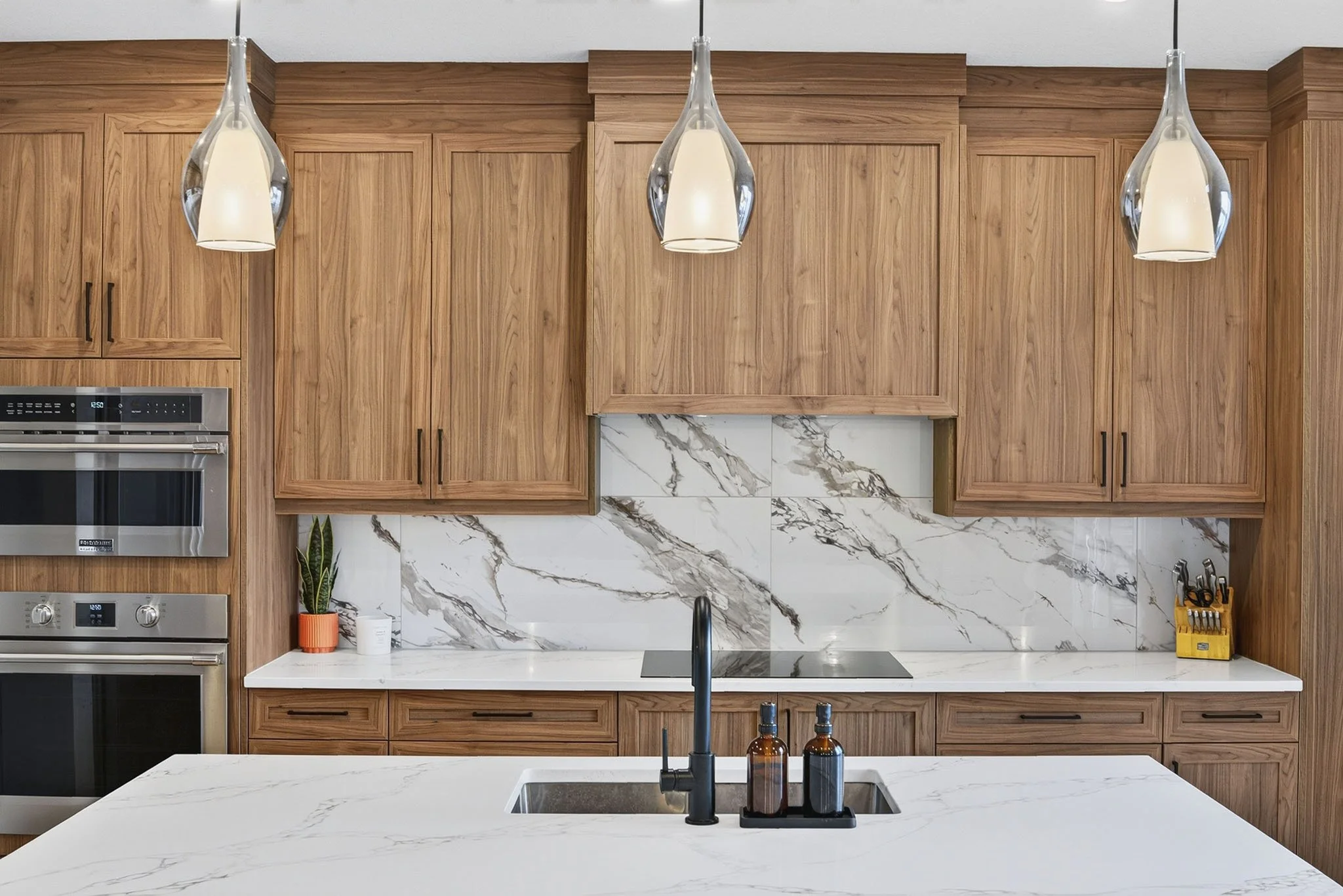 Modern kitchen with wooden cabinets, marble backsplash, pendant lights, and a white marble countertop with a sink.