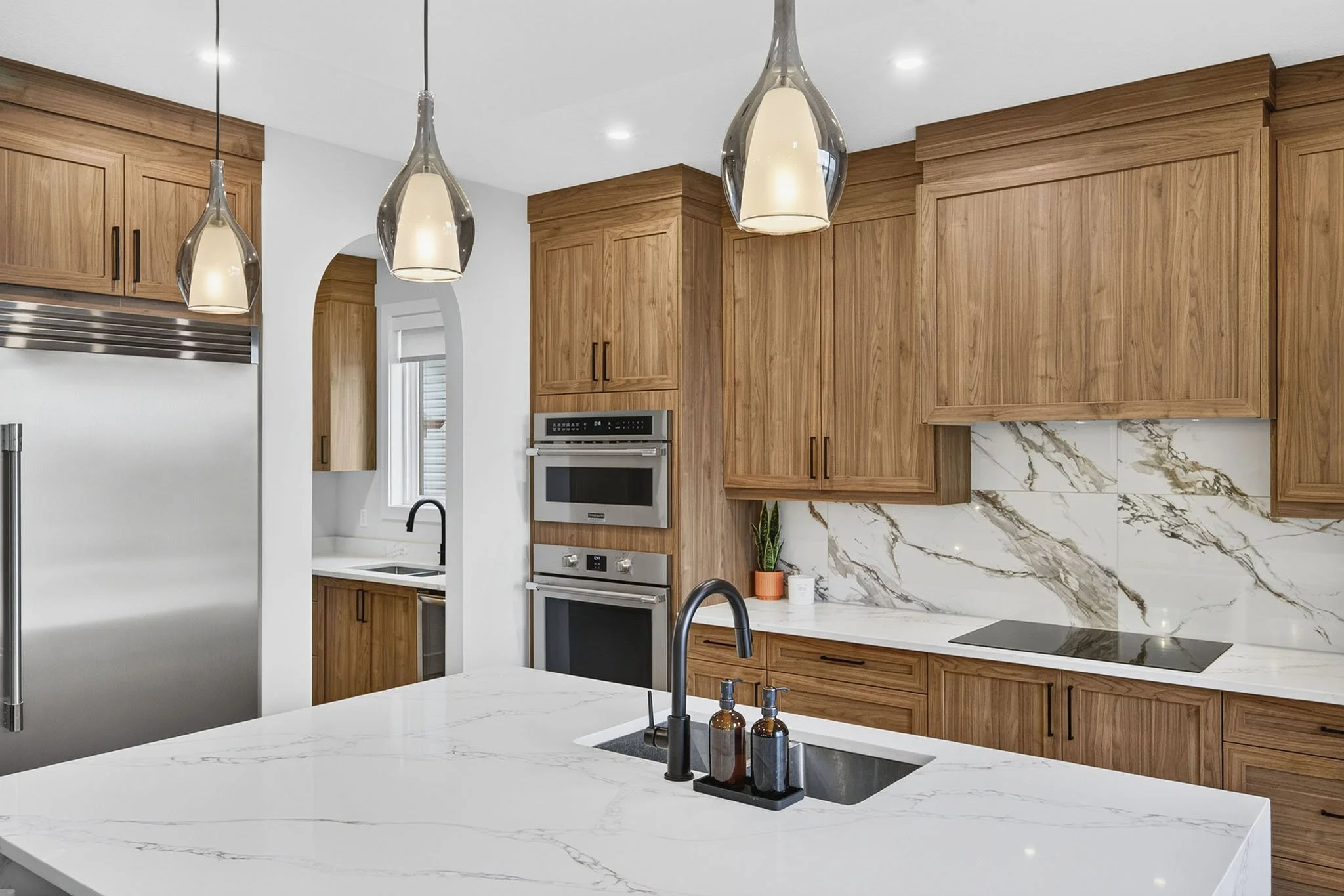 Modern kitchen with wooden cabinets, a marble backsplash, white marble island, black sink, and pendant lights.