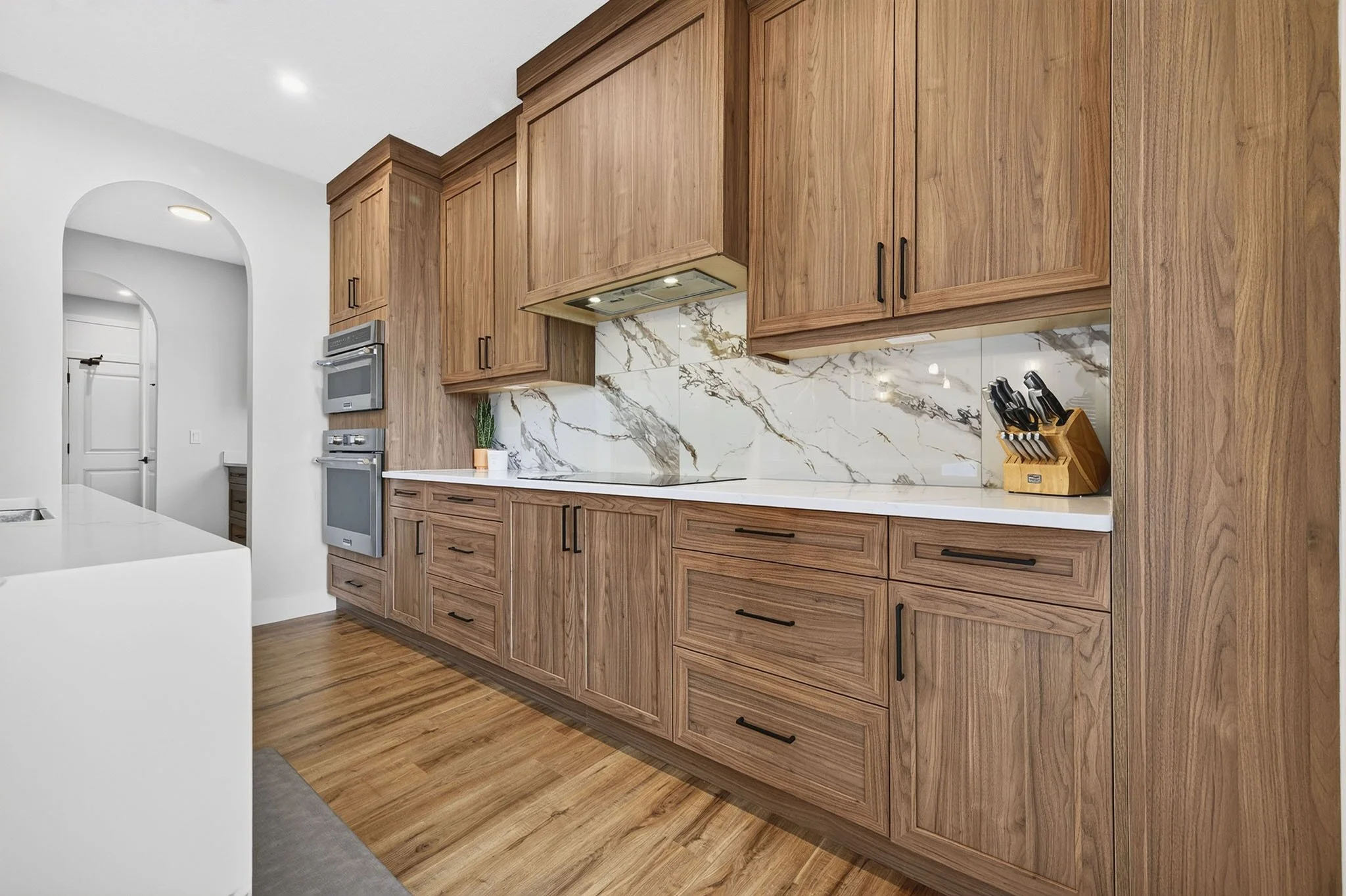 Kitchen with wooden cabinets, marble backsplash, and black handles. Contains a cutting knife set on a wooden block. Modern appliances and a potted plant are visible.