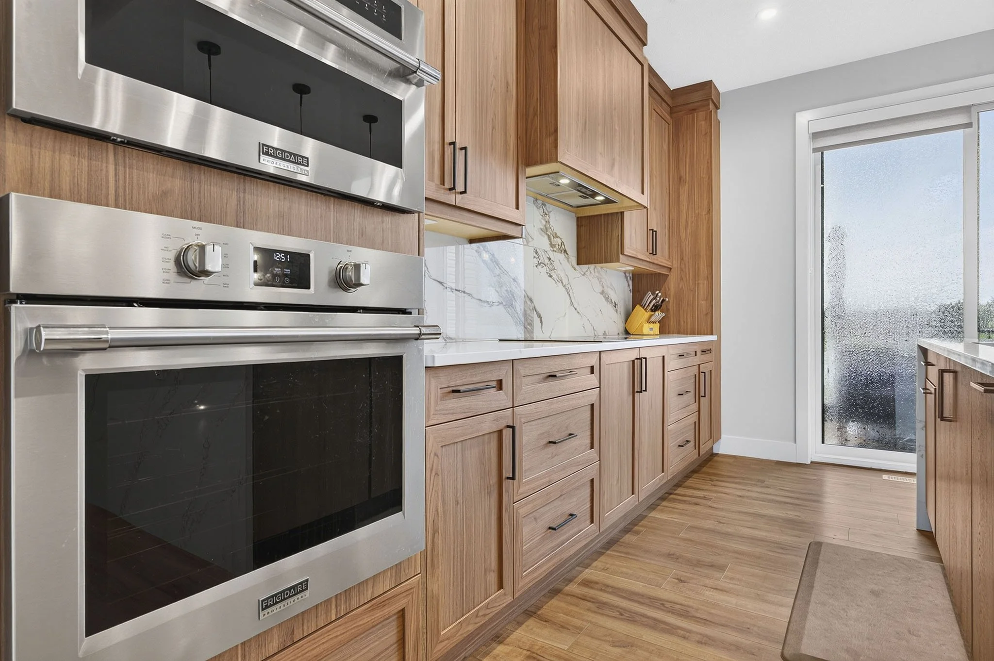 Modern kitchen with wooden cabinets, stainless steel oven, marble backsplash, and large sliding glass door leading outside