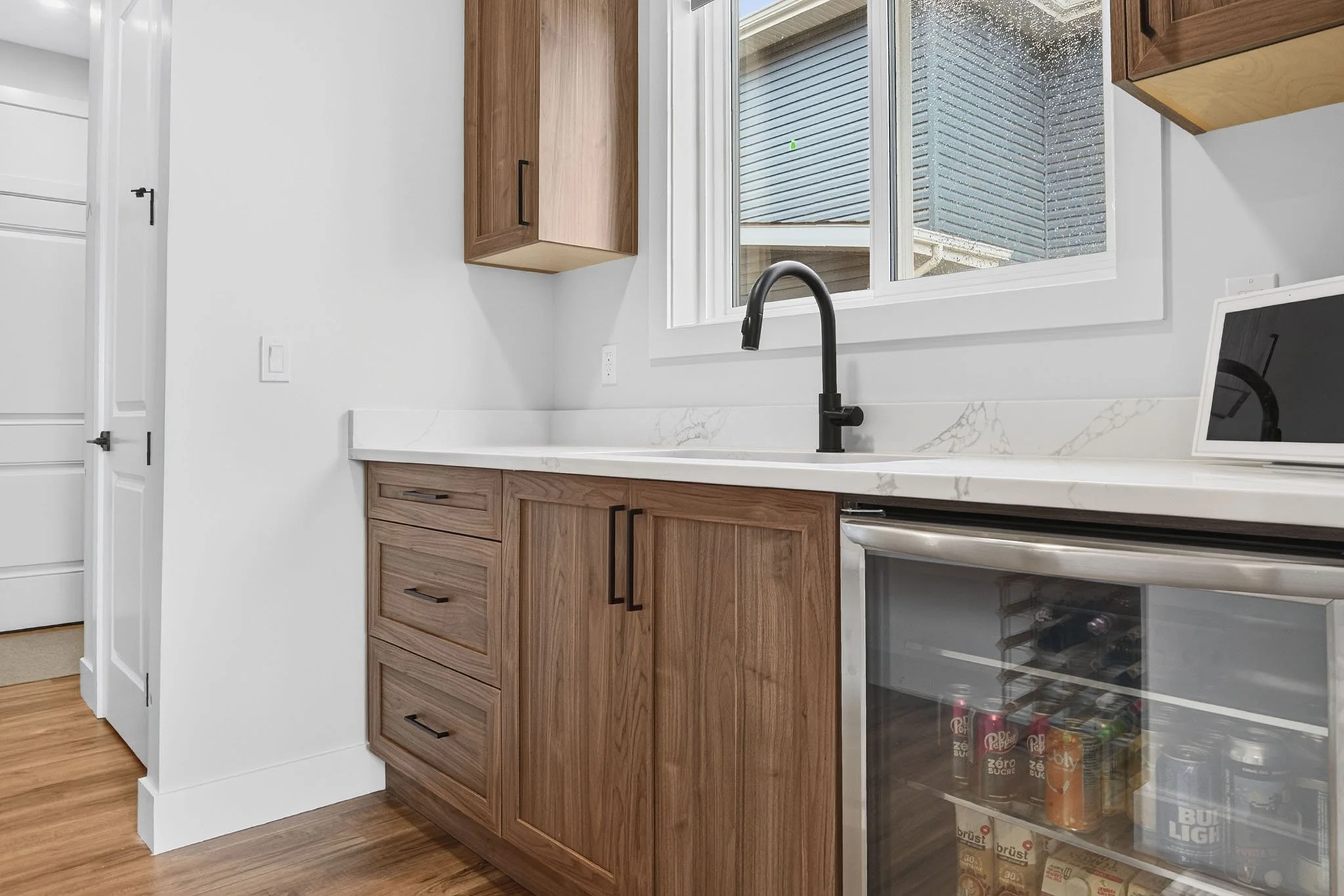 Kitchen with wooden cabinets, black faucet, white marble countertop, and a window showing an exterior building wall.