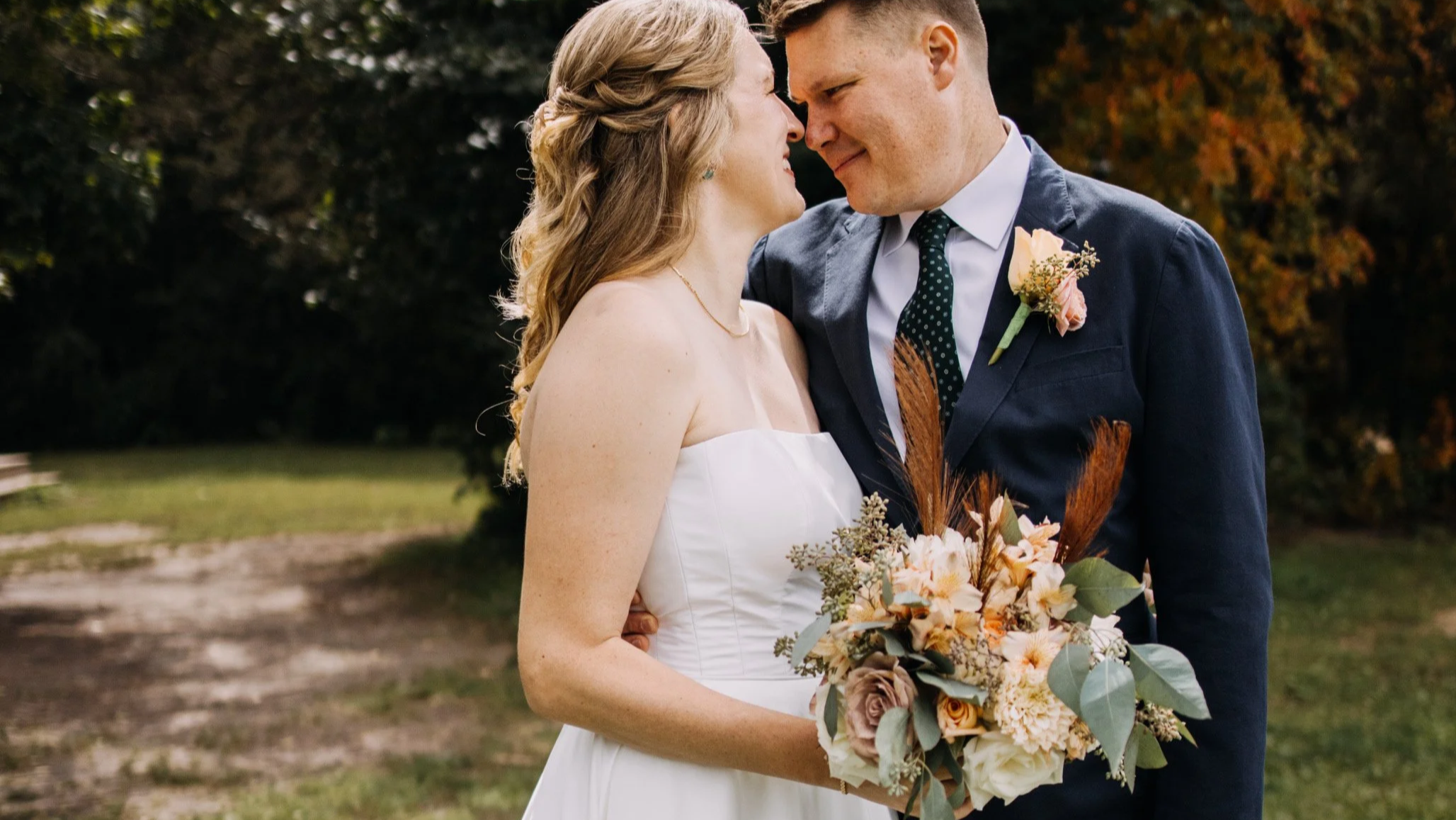 A bride and groom share a close moment outdoors on their wedding day, with the bride holding a bouquet of flowers.