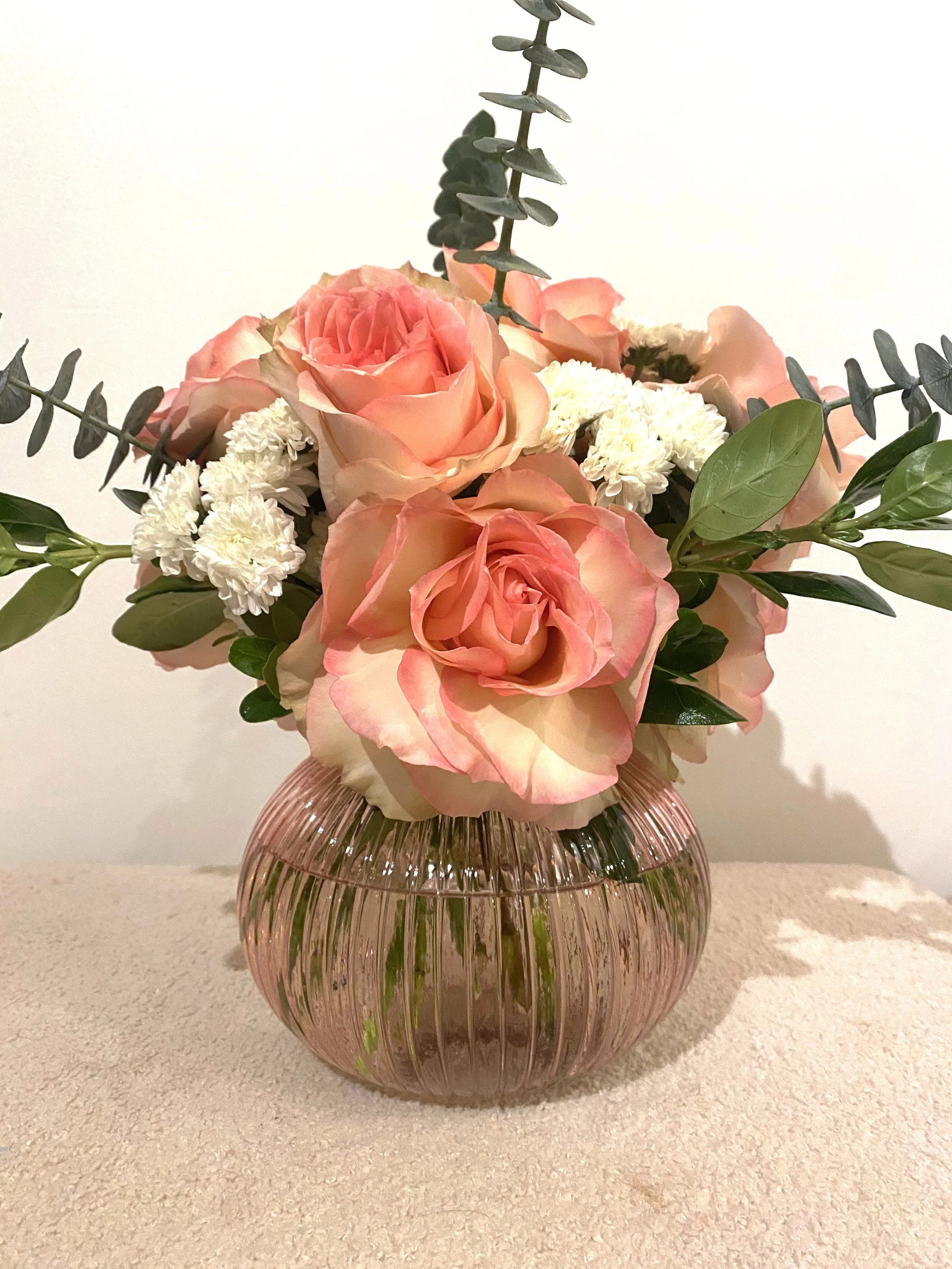 Pink and peach roses with white flowers, eucalyptus, and greenery in a ribbed glass vase.