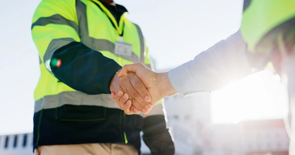 Two people shaking hands outdoors, one wearing a high-visibility vest.