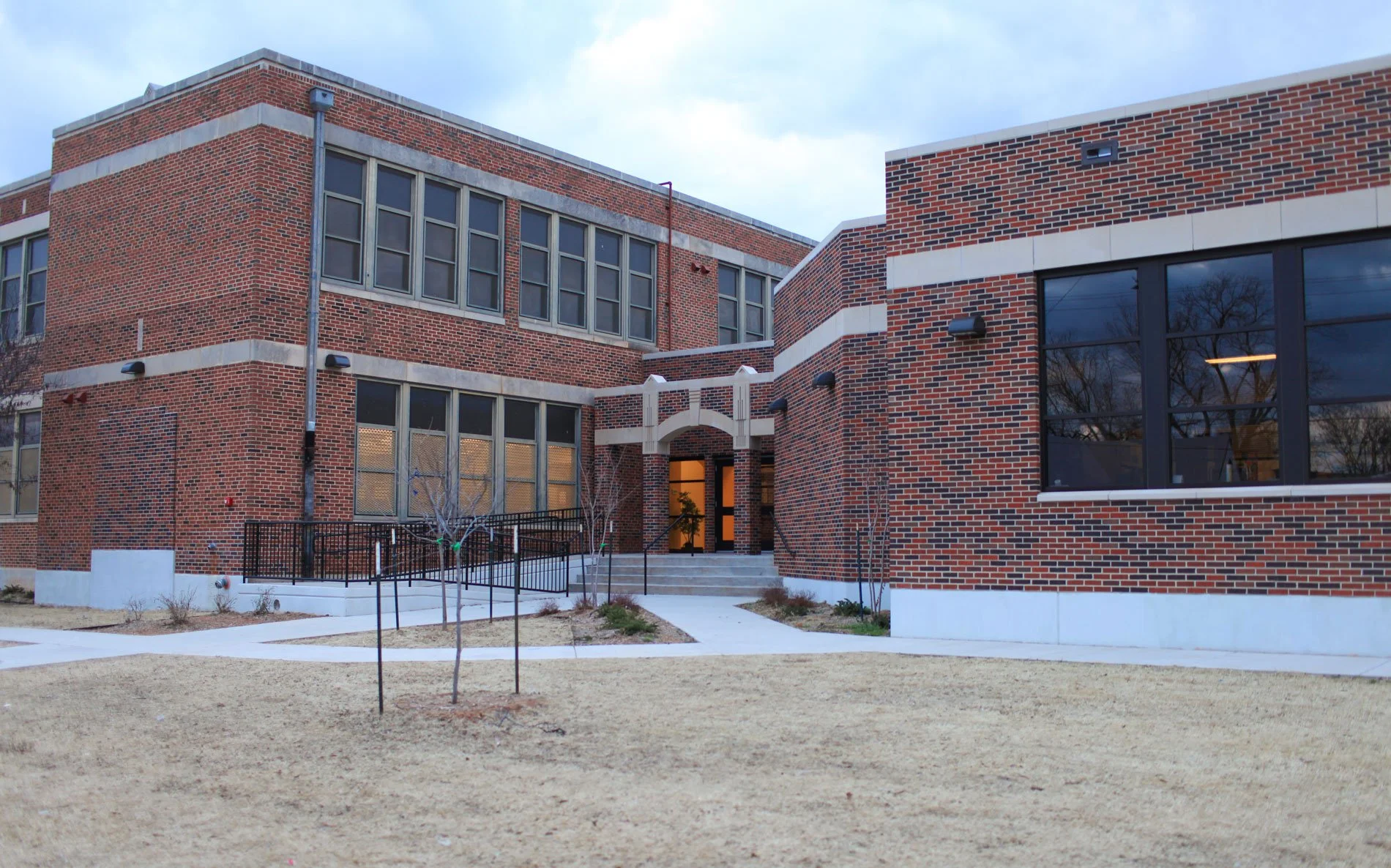 Red brick building with the sign 'HORACE MANN' above the entrance, featuring large glass doors and windows, gray sidewalk and patches of grass in front.