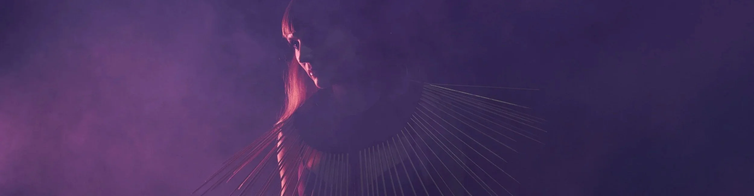 A dark, artistic image of a woman with long hair, viewed in profile, with purple and pink lighting effects and thin lines radiating outward, creating a halo-like effect.