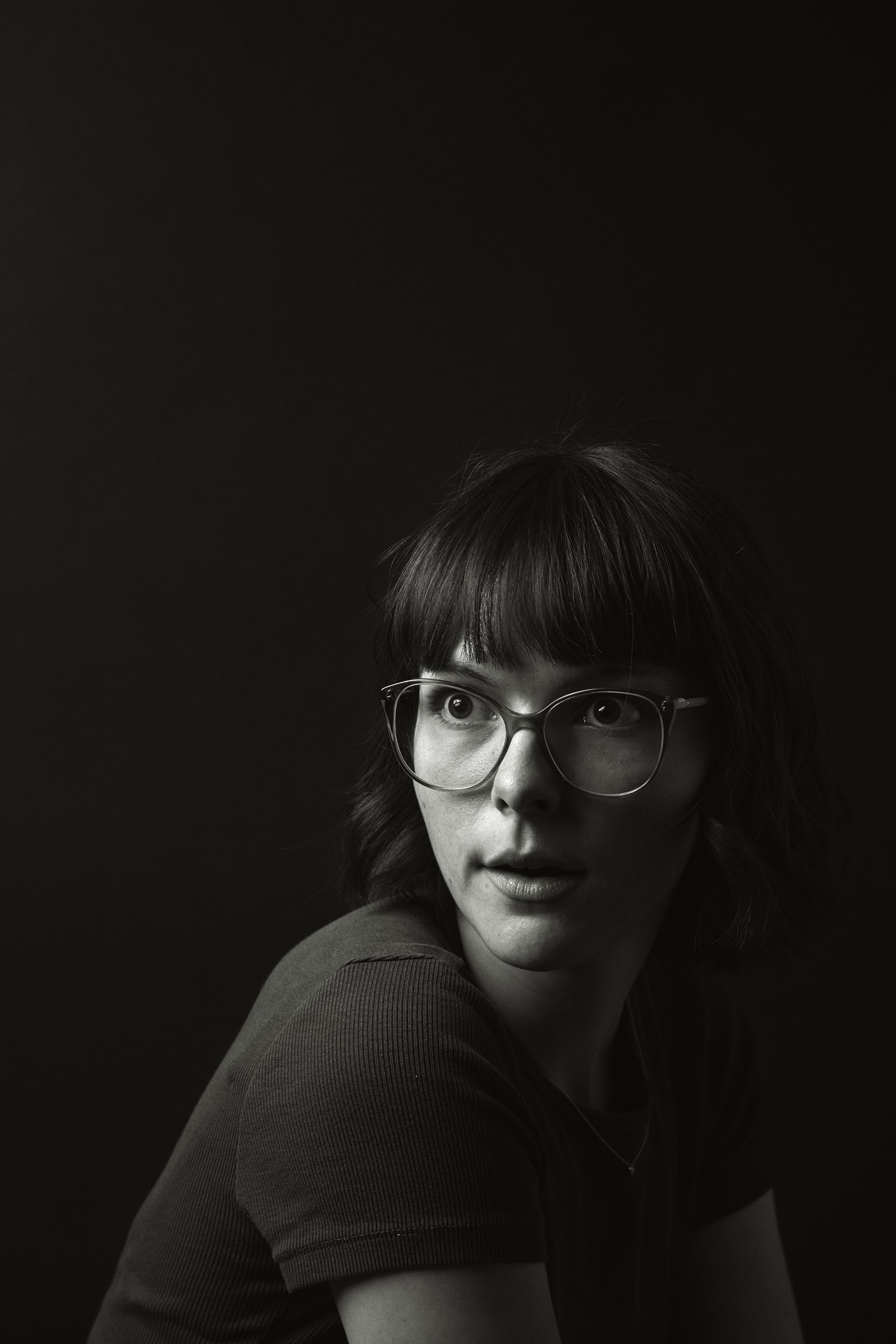 Schwarz-weiß Porträt einer Frau mit Brille, dunklem, glattem Haar und einem dunklen Oberteil, die nach rechts schaut.