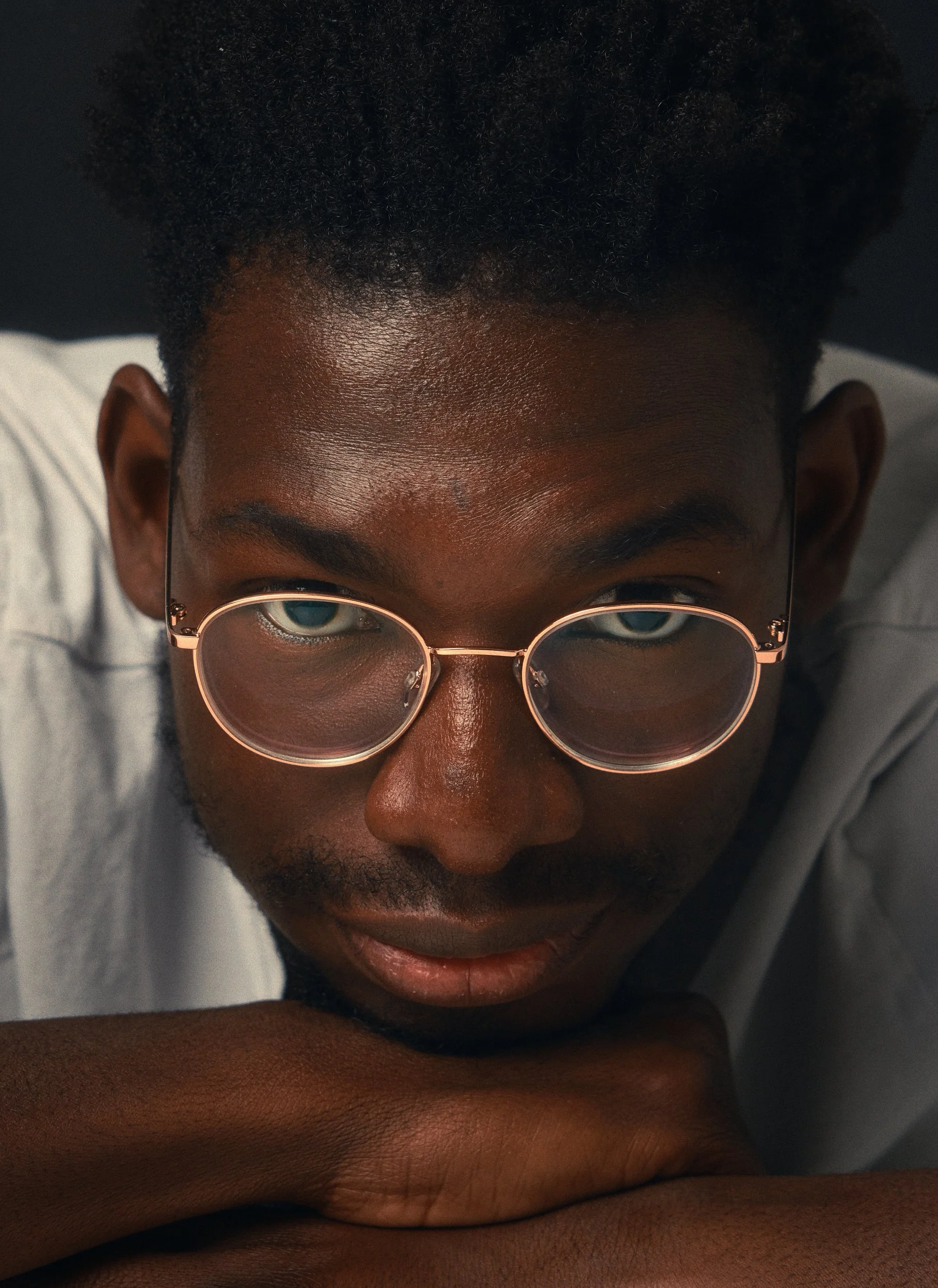 Nahaufnahme eines Mannes mit dunkler Haut, der große runde Brillen trägt, die Augen sind sichtbar durch die Brille, die Haare sind lockig und schwarz.