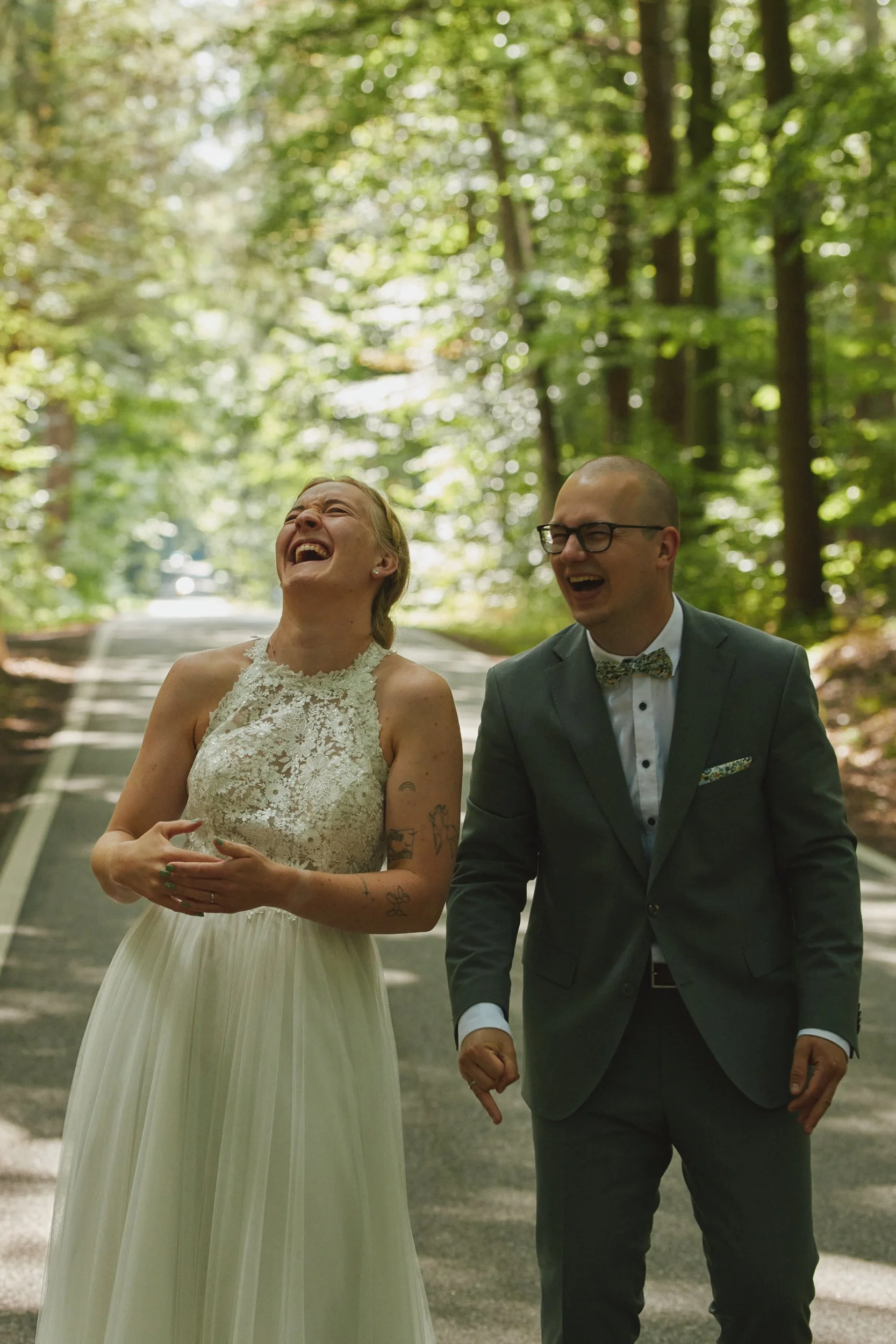 Ein Paar, wahrscheinlich Braut und Bräutigam, lachen und gehen zusammen in einem Wald, vermutlich an ihrem Hochzeitstag.