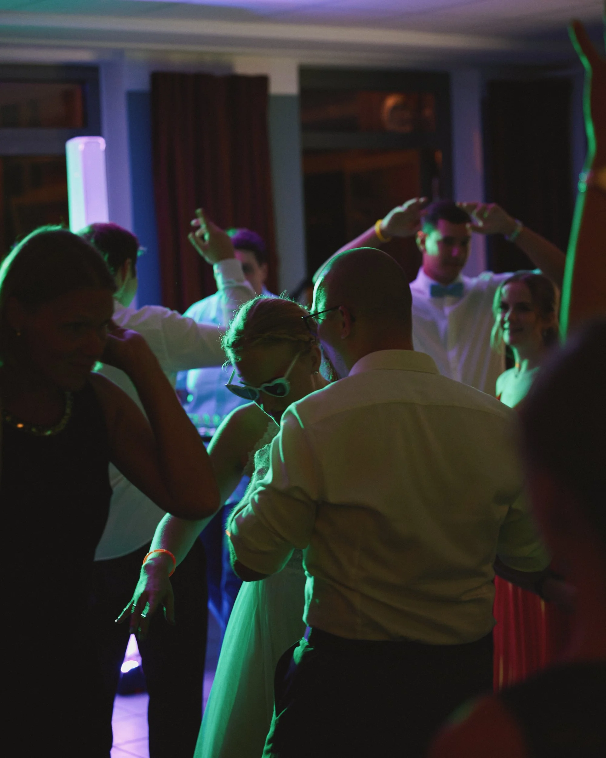 Menschen tanzen zu Musik bei einer Party, beleuchtet mit bunten Neonlichtern.