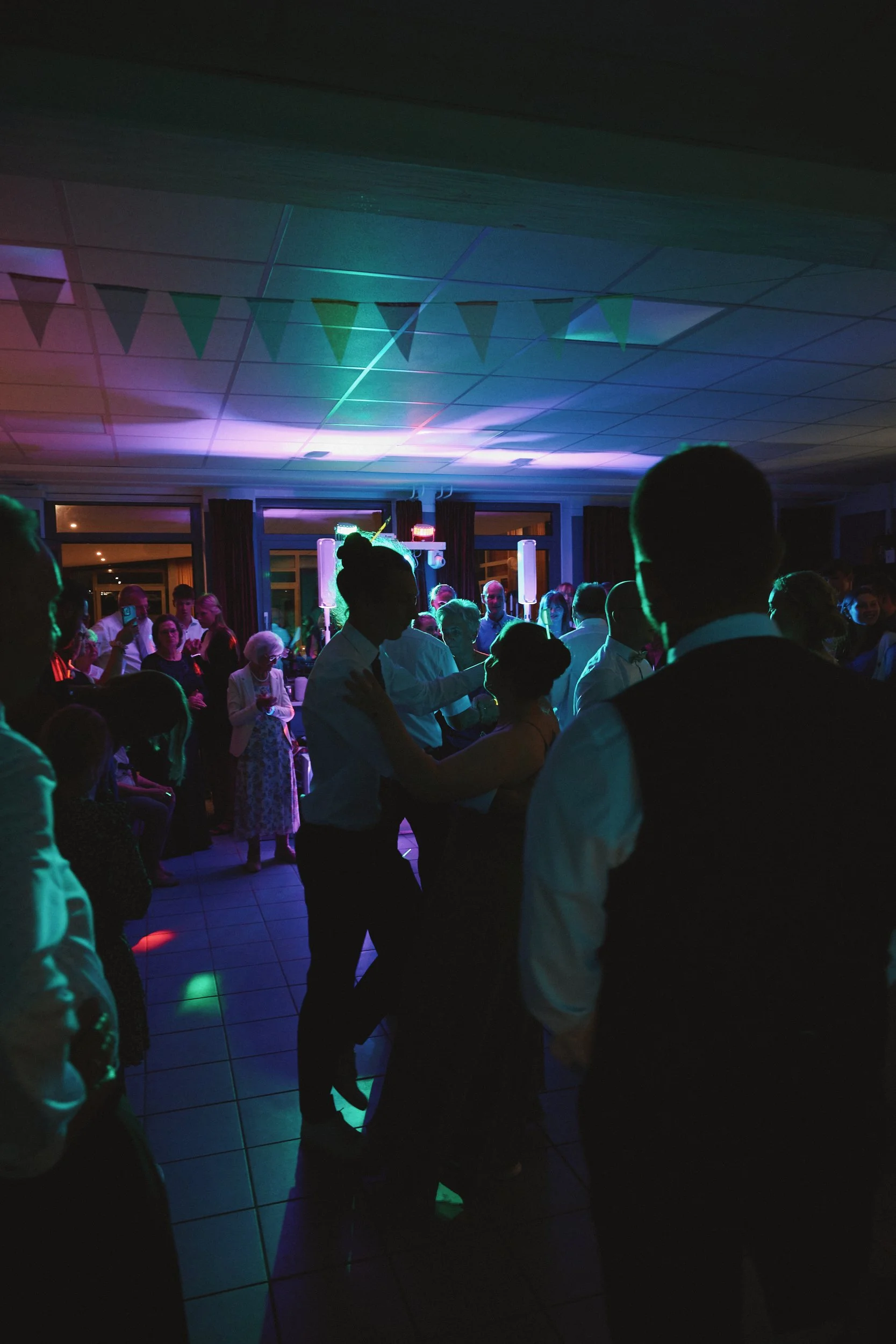 Menschen tanzen in einem dunklen Raum mit bunten Lichtern und Girlanden an der Decke, vermutlich bei einer Feier oder Party.