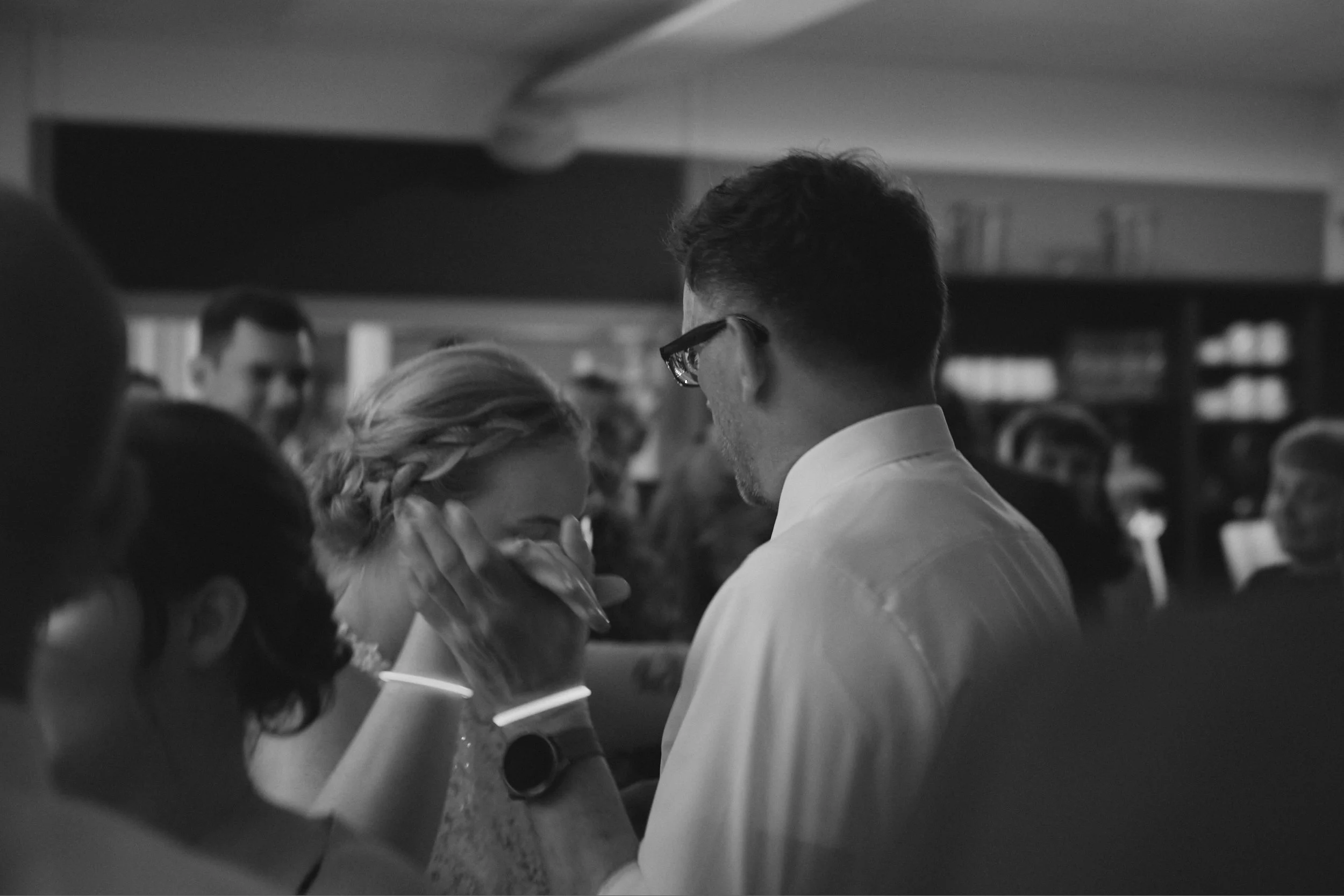 Schwarze und weiße Fotografie in einer Küche, Menschen in Gesprächen, eine Frau mit Zopf und ein Mann mit Brille haben ein Gespräch.