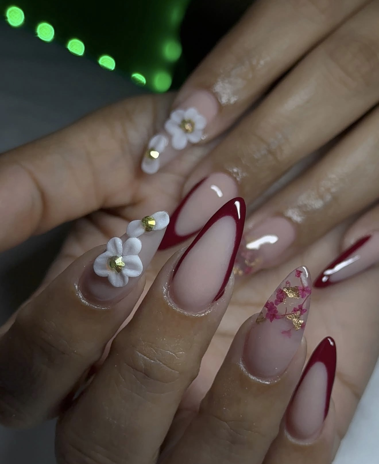 Close-up of hands with manicured nails featuring floral, red, and gold designs, and 3D flower and bead embellishments.