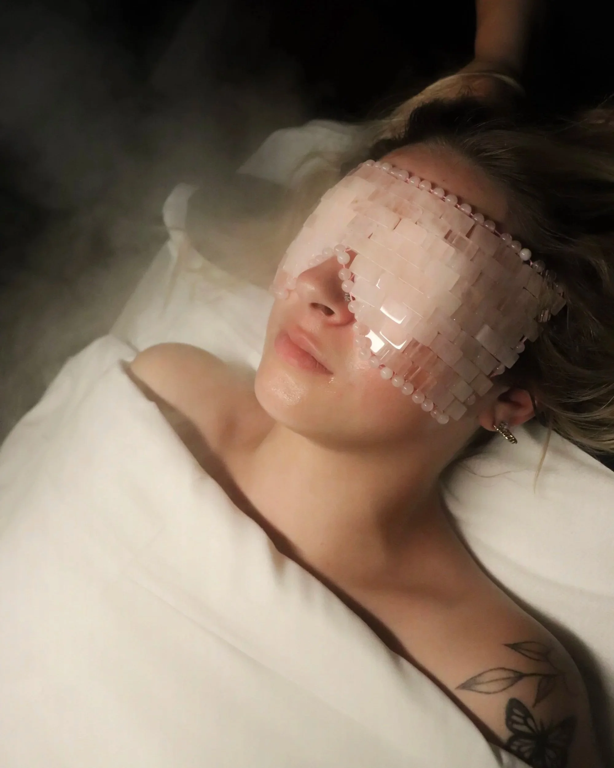 Close-up of a woman lying in bed wearing decorative glasses, with a tattoo of butterflies on her arm.