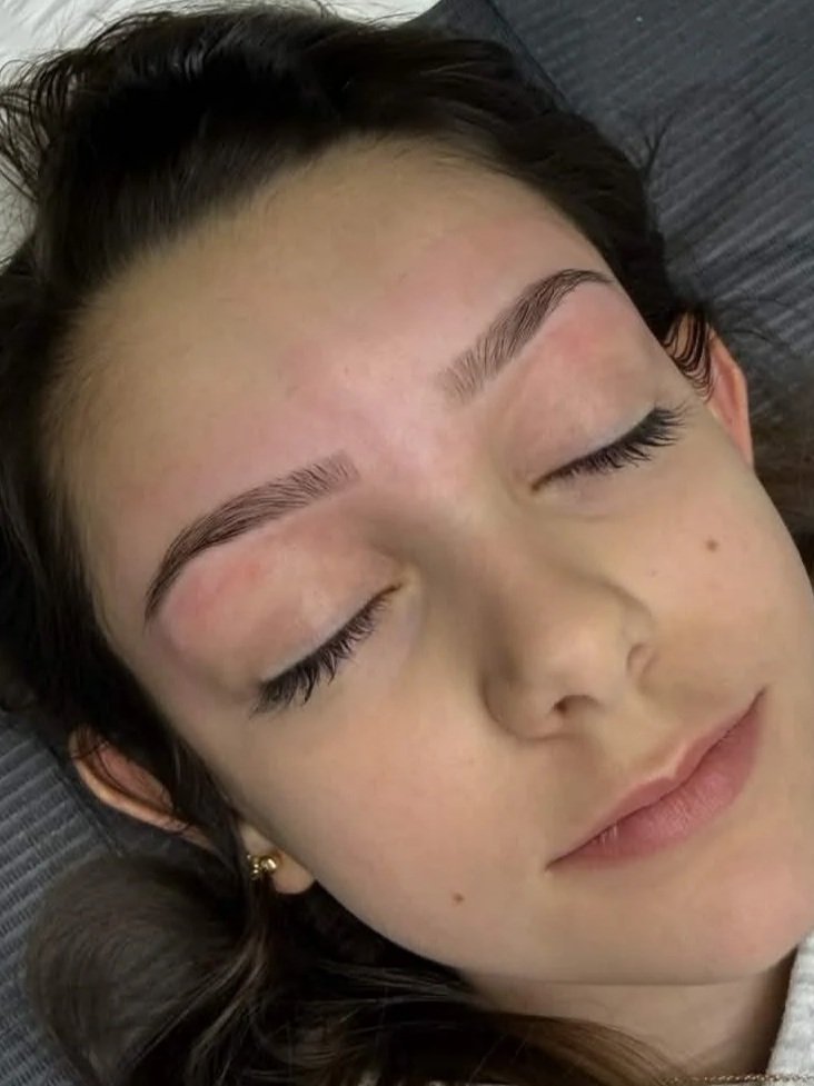 Close-up of a young woman with fair skin and dark hair, lying down with her eyes closed, relaxing.