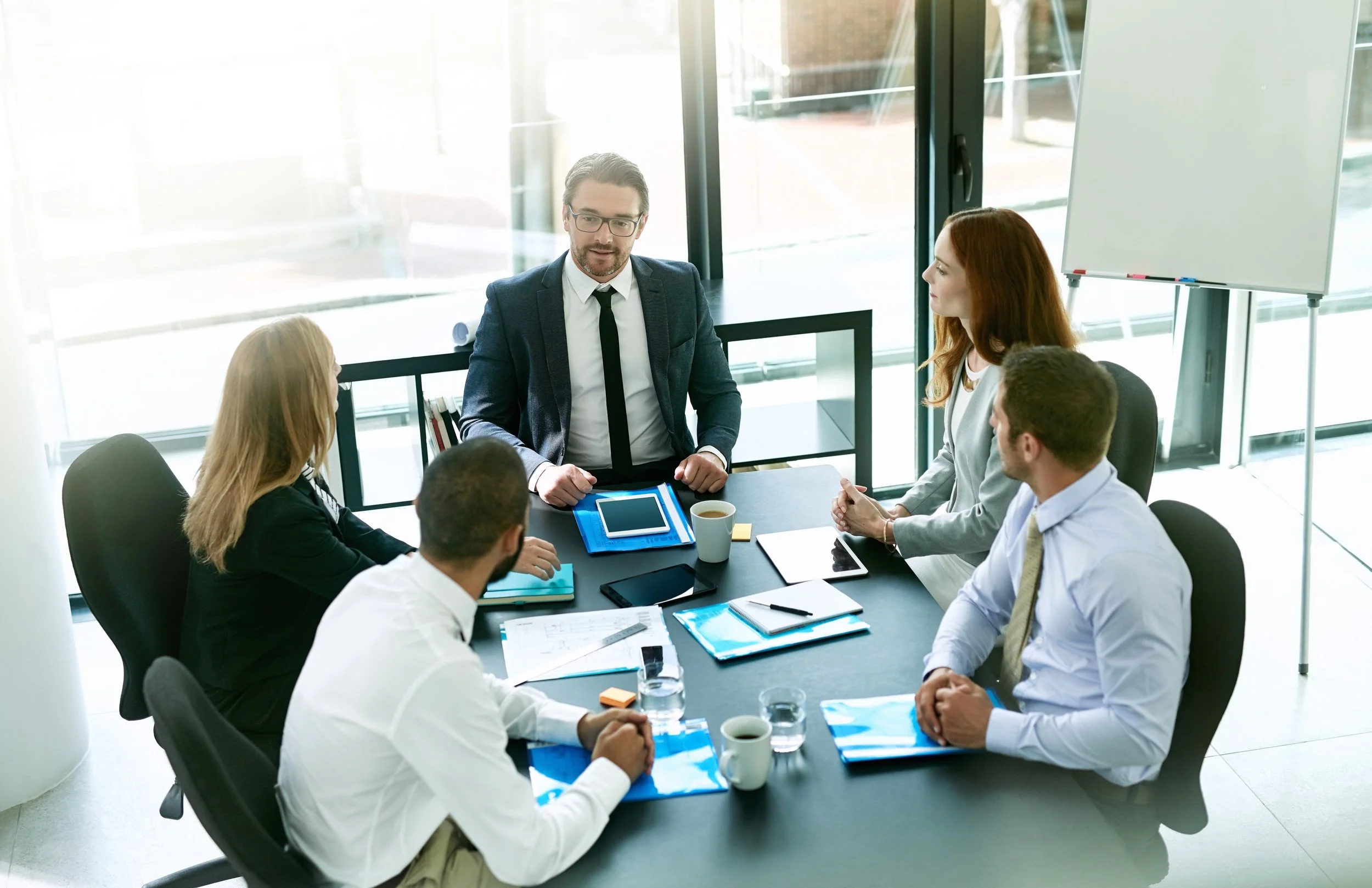 Business meeting with a man in a suit addressing four colleagues in a conference room.