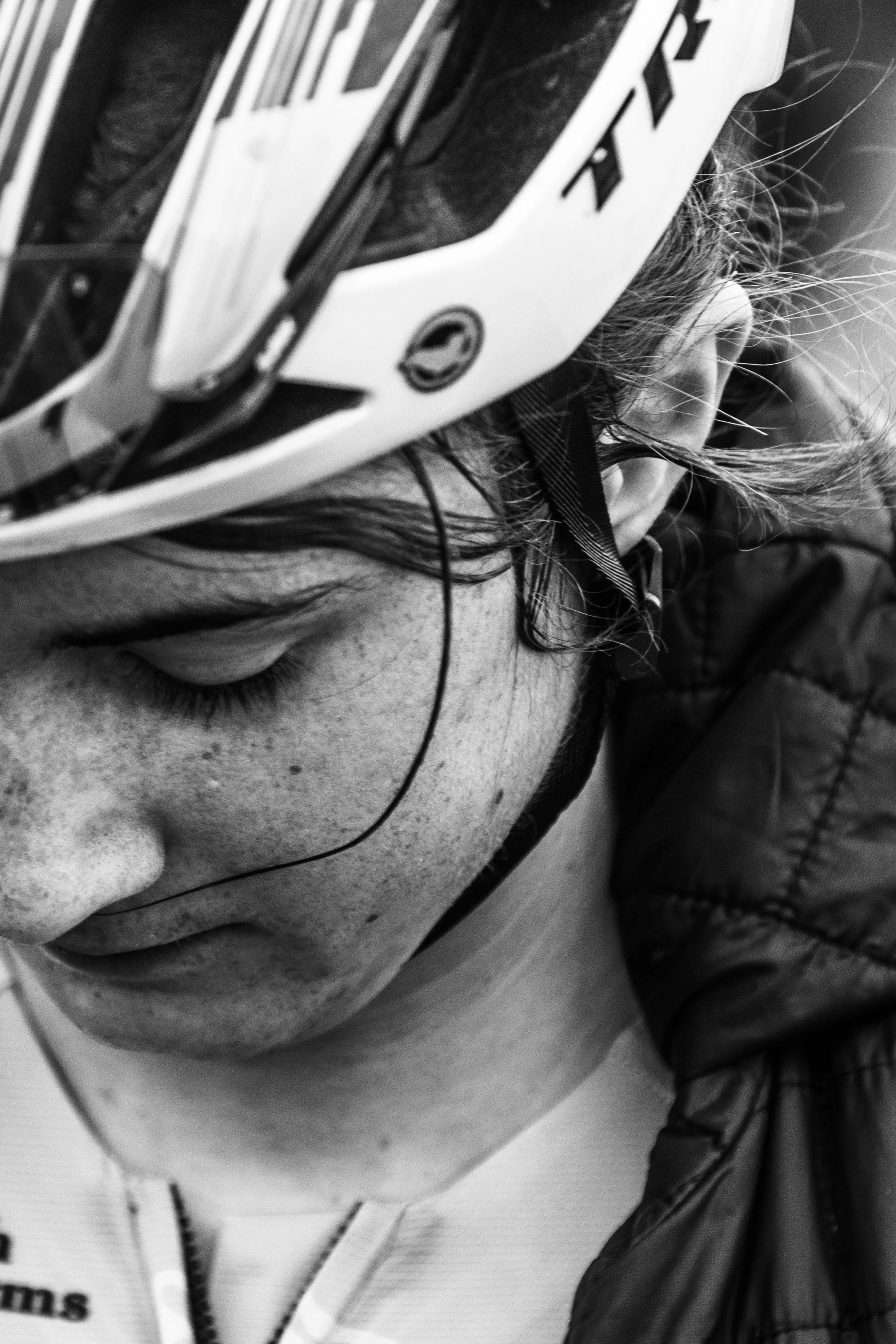 Close-up of a young woman in a helmet with eyes closed, freckles visible, wearing a jacket and a hoodie.