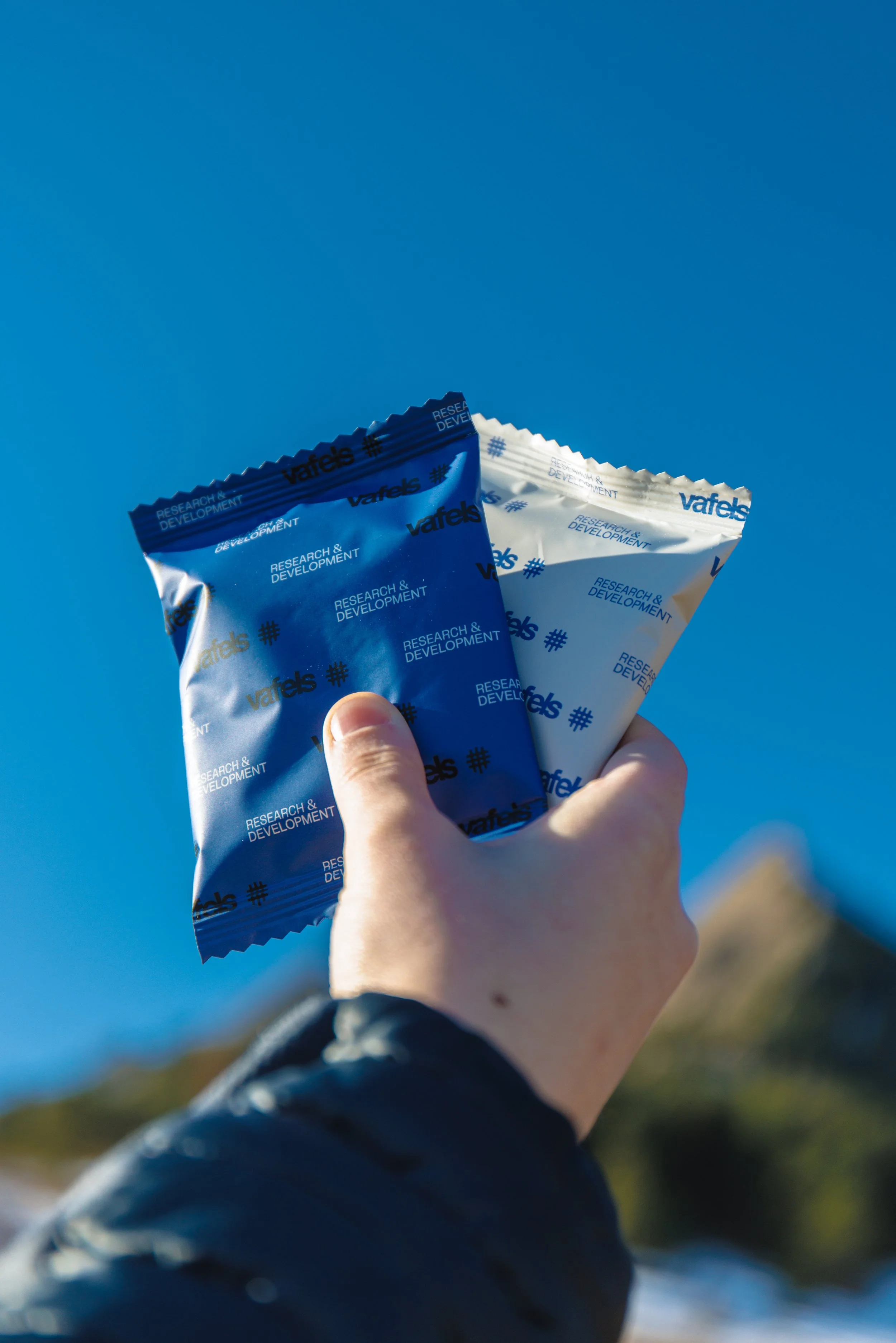 Hand holding two Vafels-branded research and development stroop waffles against a blue sky background.