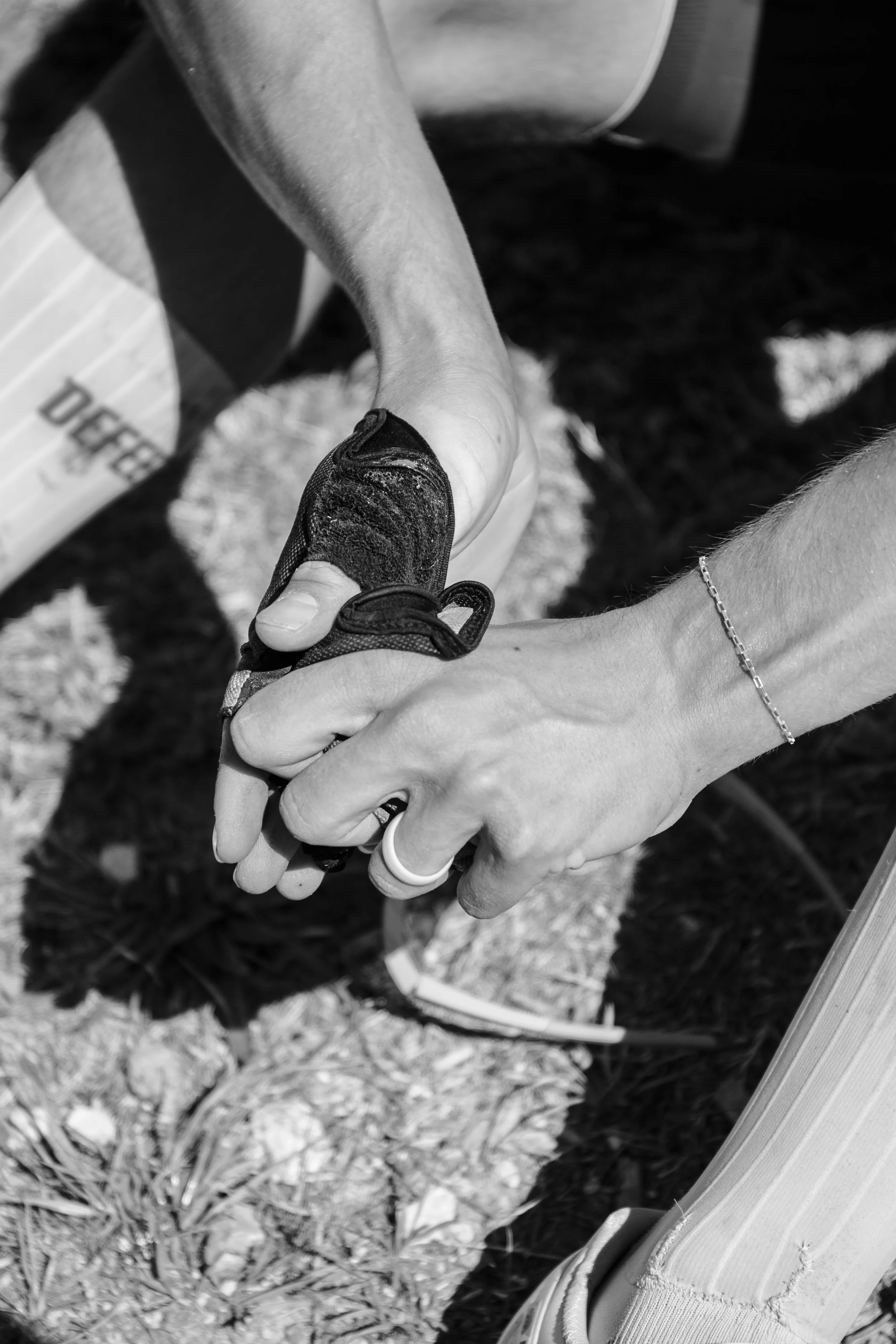 Athlete outdoors on rocky ground, removing gloves from dusty hands.