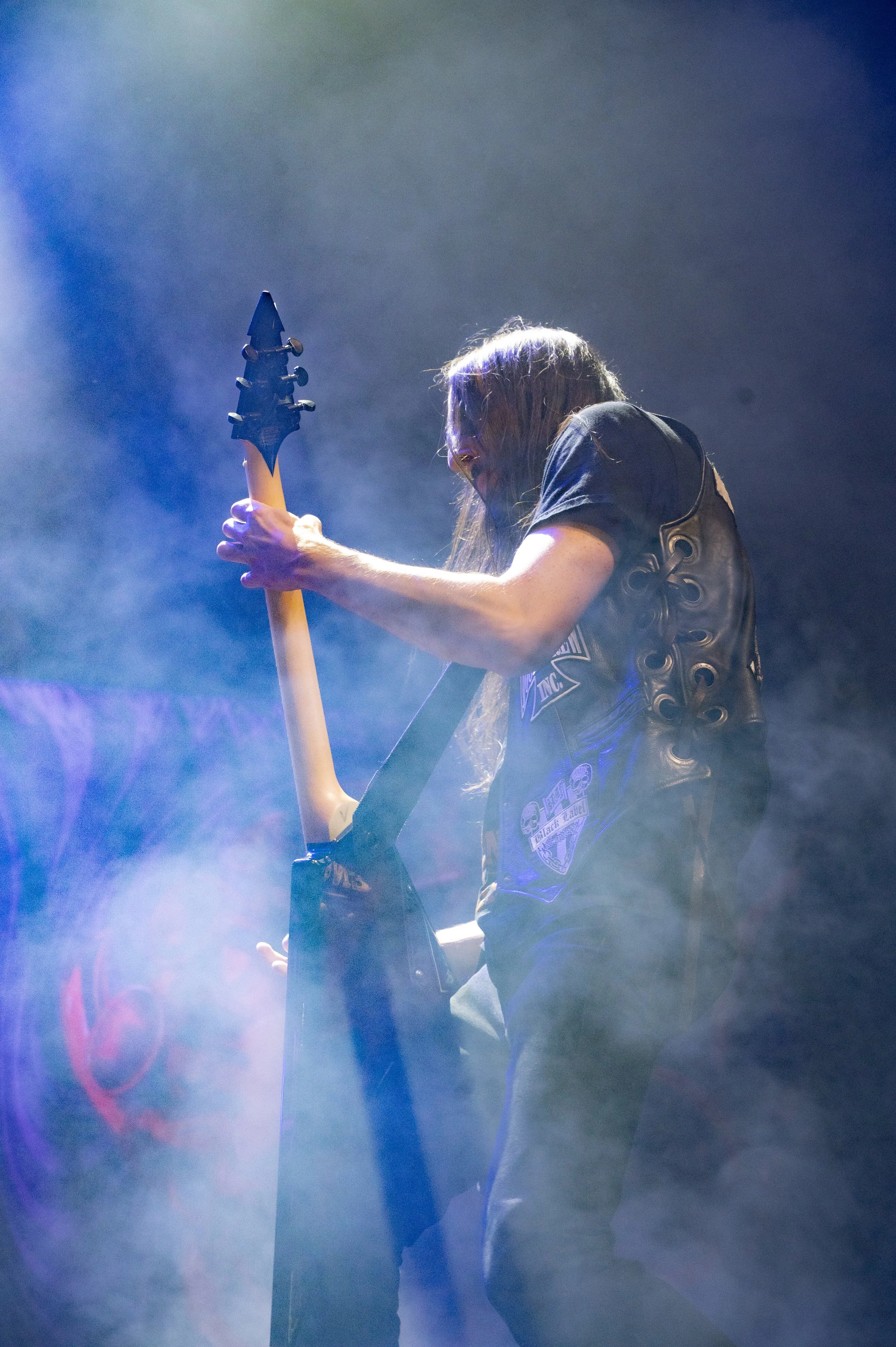 A guitarist playing electric guitar on stage with smoke and colorful lights.