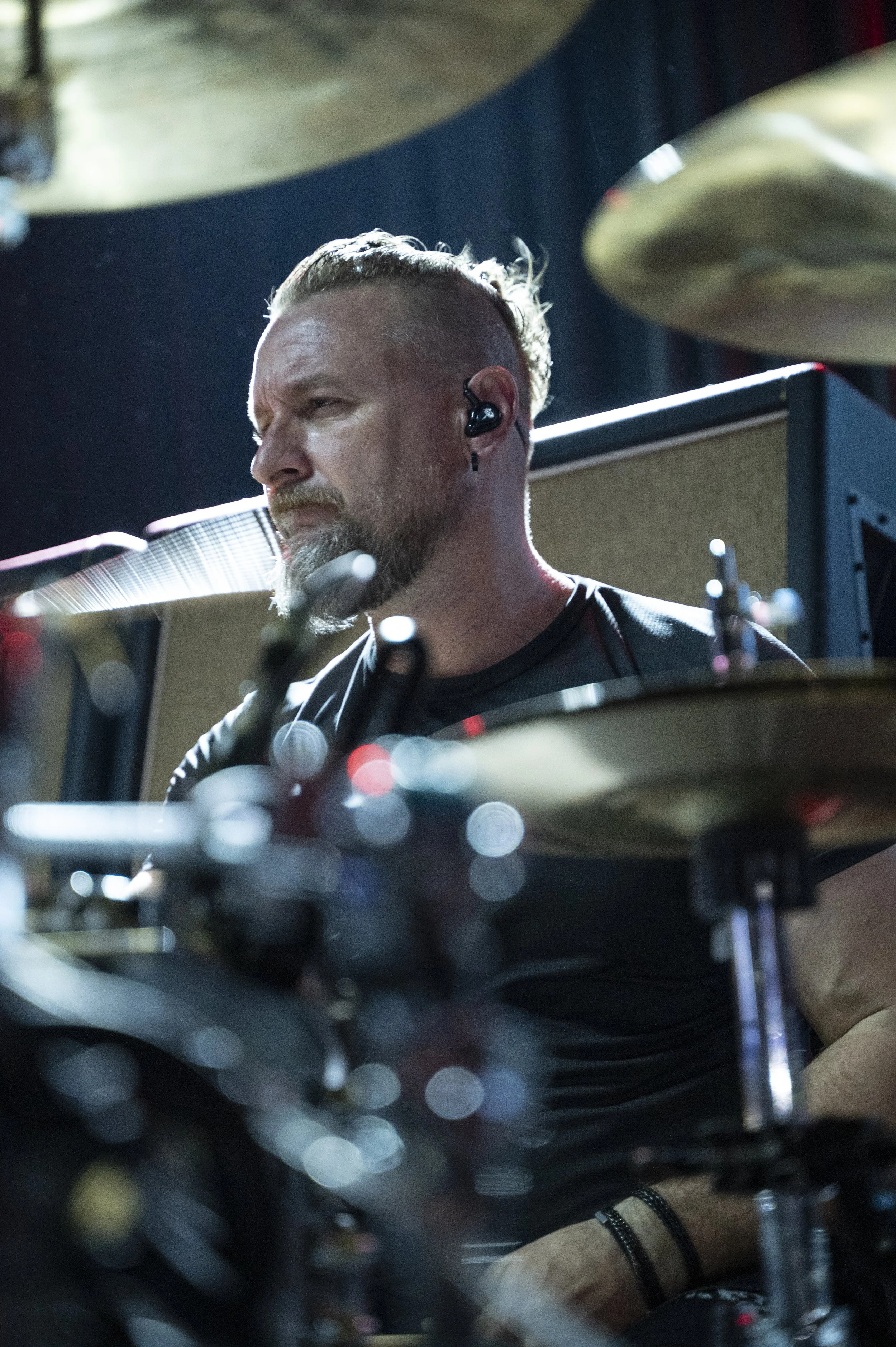 A male drummer with a beard and earphones, focused while playing drums during a live performance.