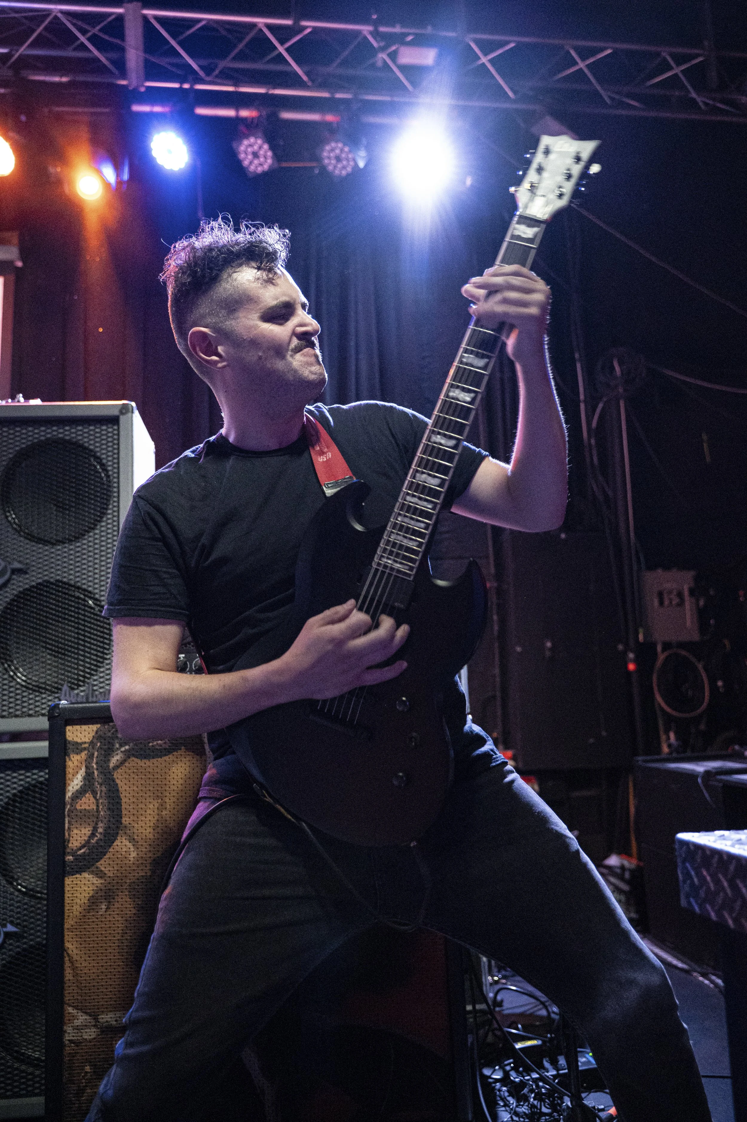 A person playing an electric guitar on stage with colorful concert lighting.