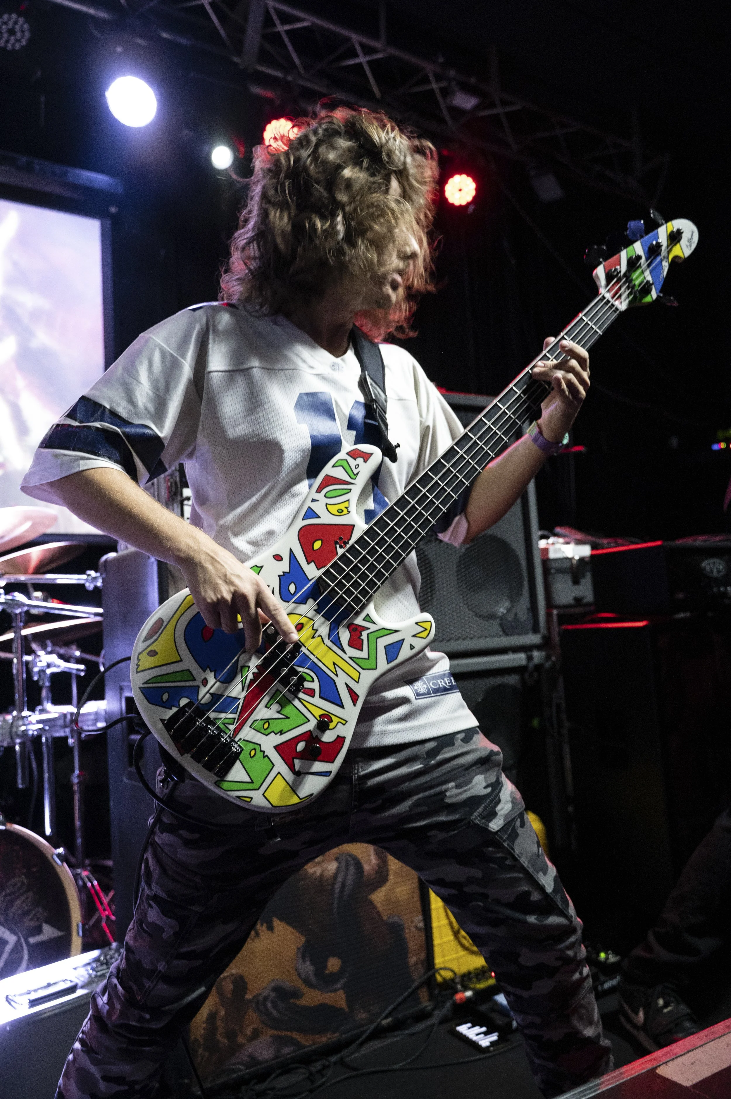 A musician playing an electric bass guitar with a colorful graffiti design on it during a live performance on stage.