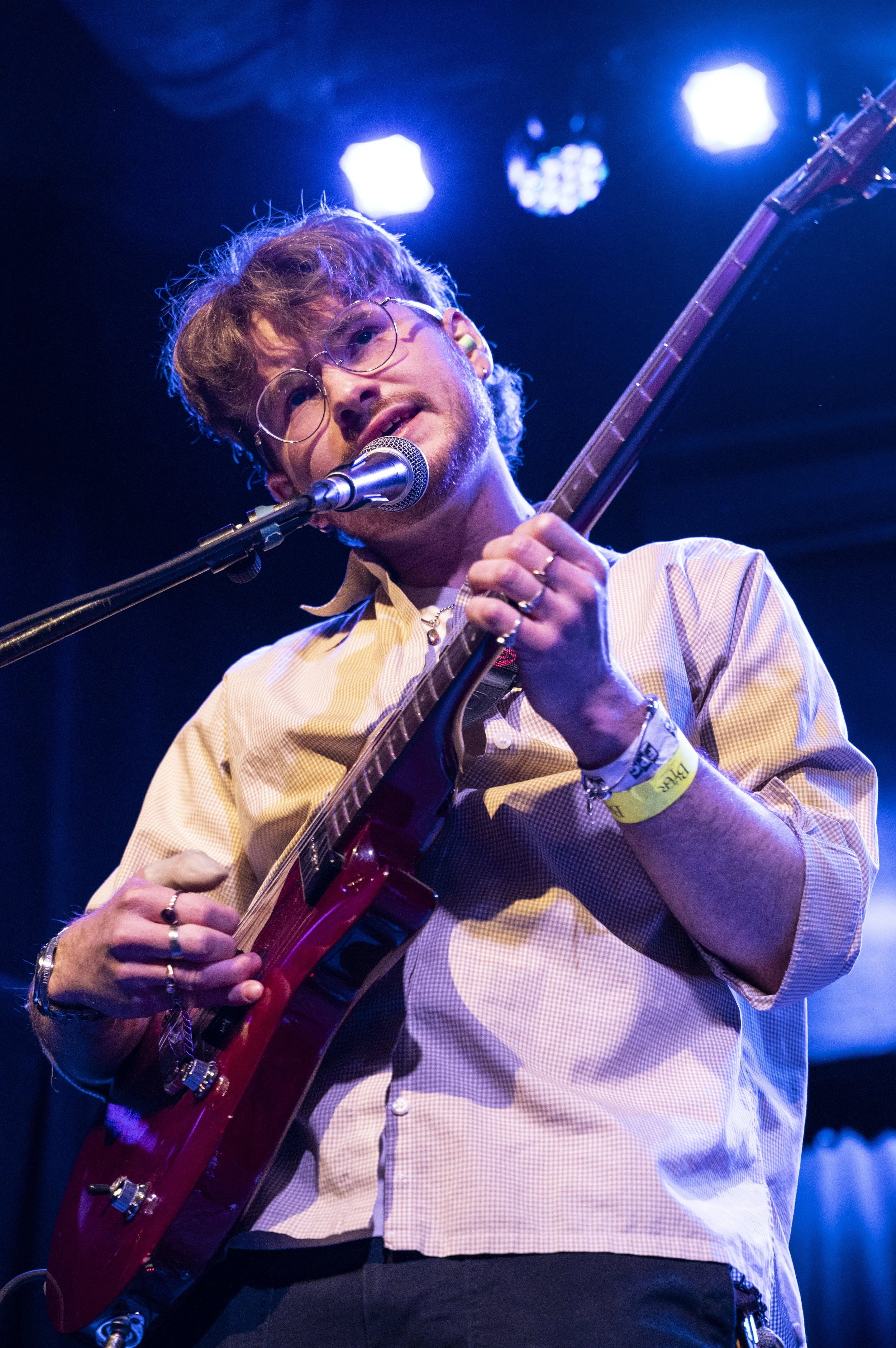 Musician performing on stage with an electric guitar, singing into a microphone under blue stage lighting.