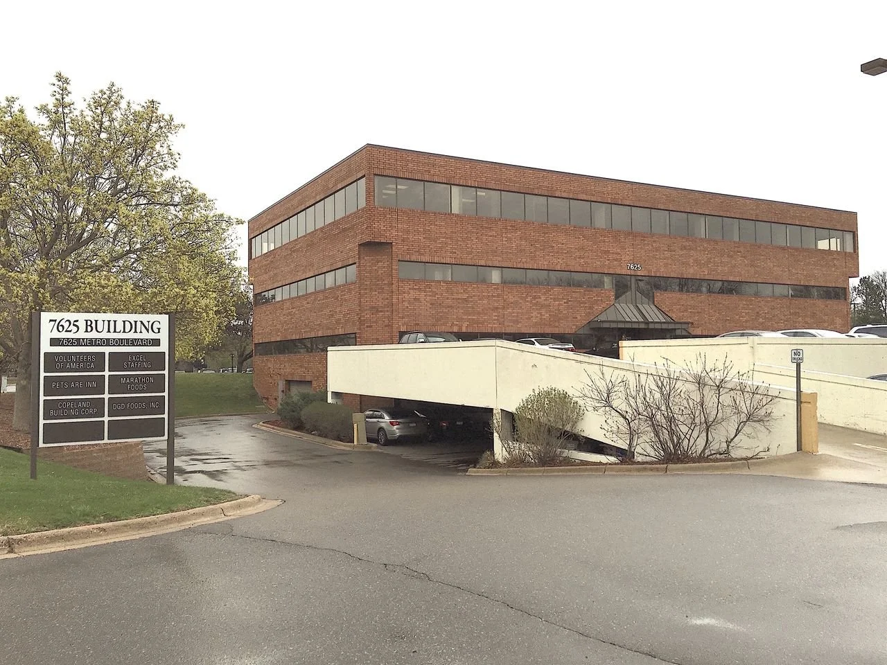 A brick office building with the address 7625 on a sign on the front, with parking on the side and a ramp leading to the parking garage underneath.