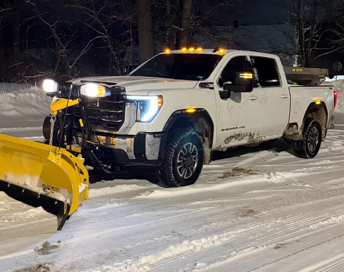 A white pickup truck equipped with snow plow on a snowy road at night.