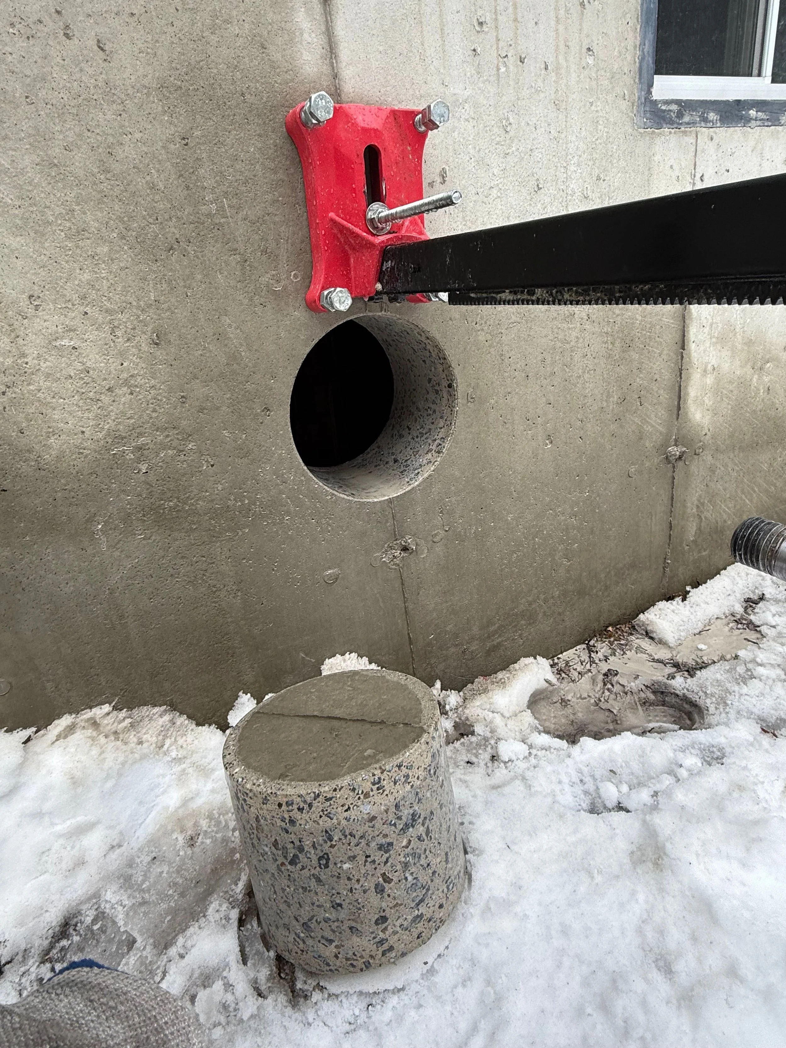 Construction site with a concrete wall, a pipe opening, and a concrete cylinder on snowy ground.
