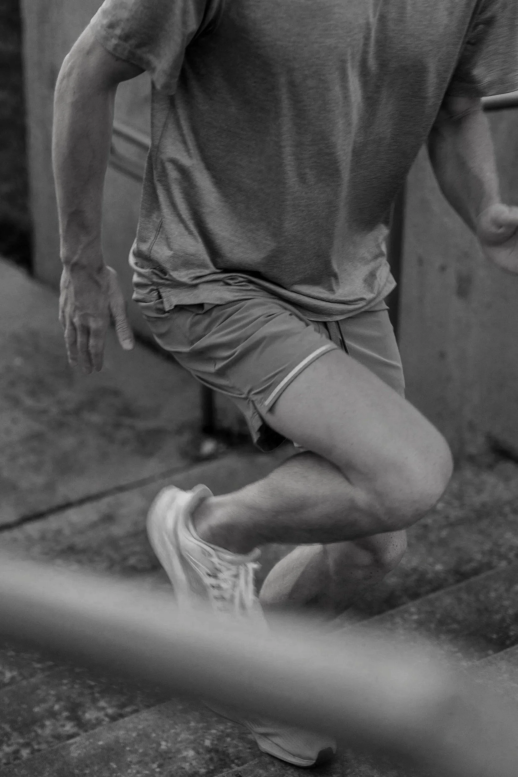 A person in athletic clothing and sneakers is kneeling or crouching on the ground, possibly preparing for or engaging in a workout or exercise in an indoor setting.