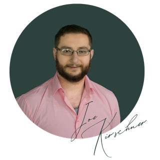Portrait of a man with glasses and a beard, wearing a light pink shirt, against a dark background.
