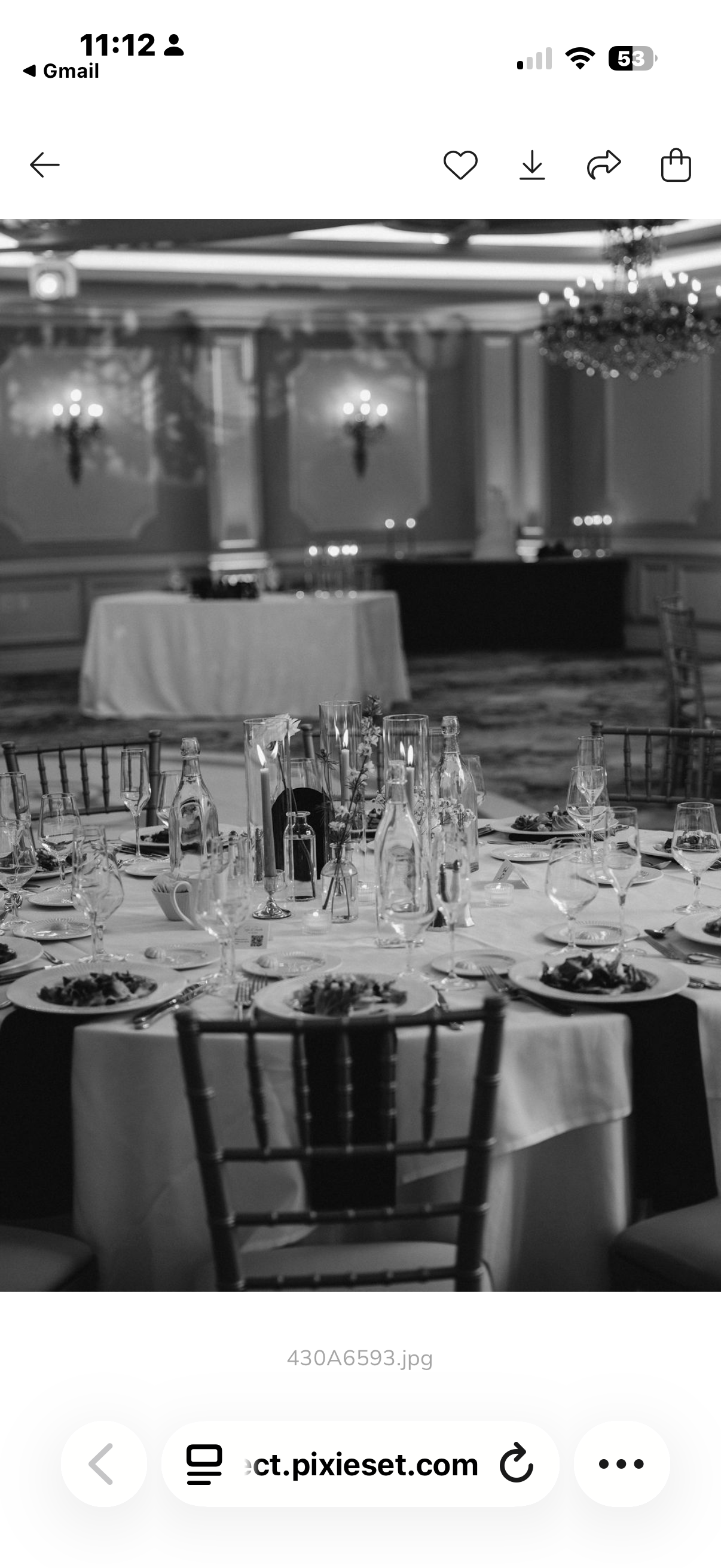 A black and white photograph of a banquet hall with a round table set for dining, featuring plates, glasses, and silverware, with a decorated centerpiece, and a large, empty dessert table in the background.