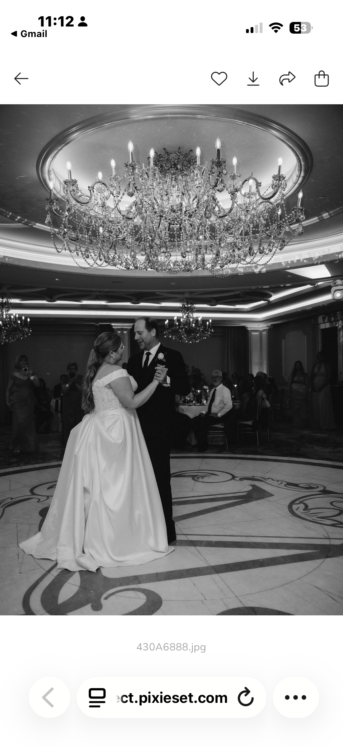 A bride and groom dance at their wedding reception under a large chandelier in an elegant ballroom filled with guests.