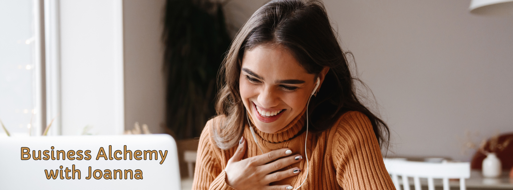 A woman in a brown sweater smiling and talking during a video call on her laptop, with the text 'Business Alchemy with Joanna' overlaid.
