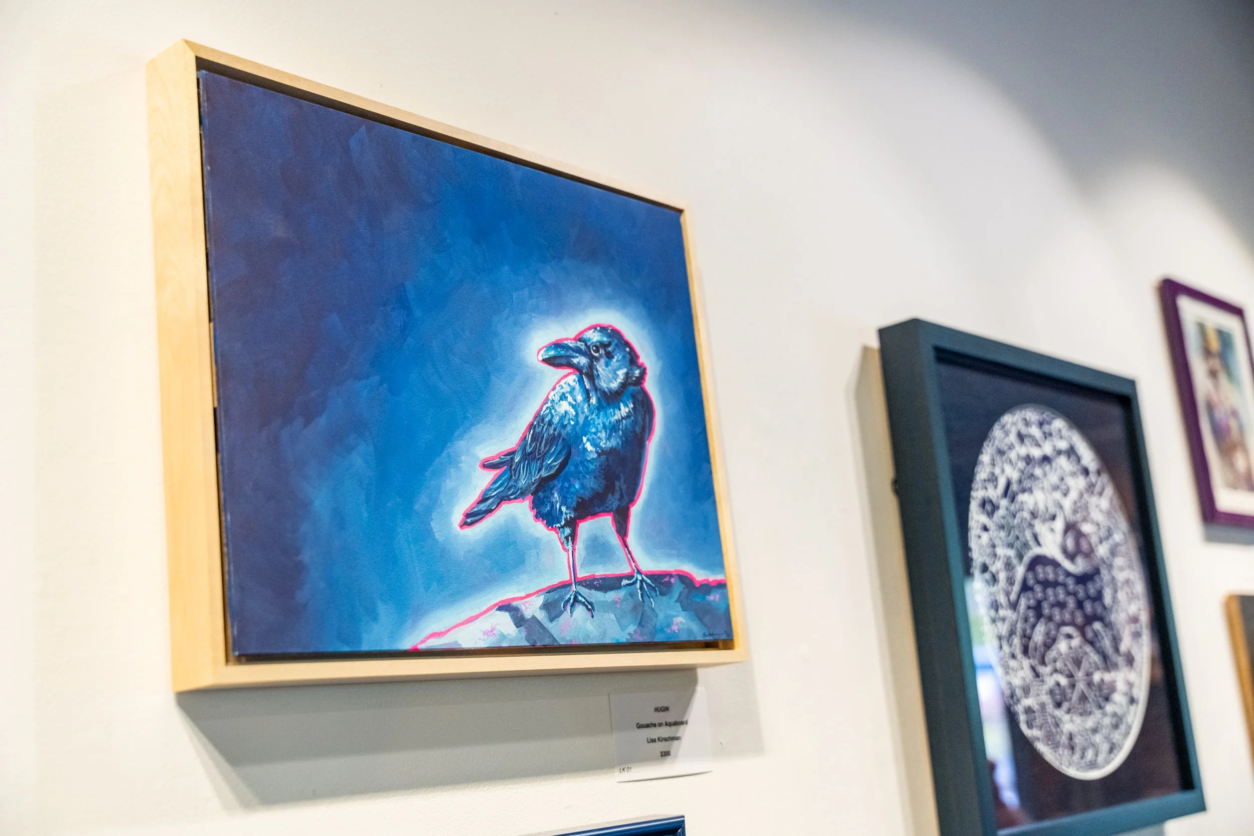 Artwork of a black bird with bright red and neon pink outlines on a blue background, hanging on a gallery wall.