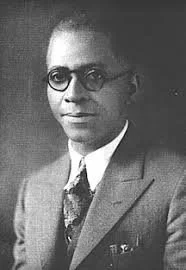 Black and white portrait of a man wearing glasses and a suit with a tie.